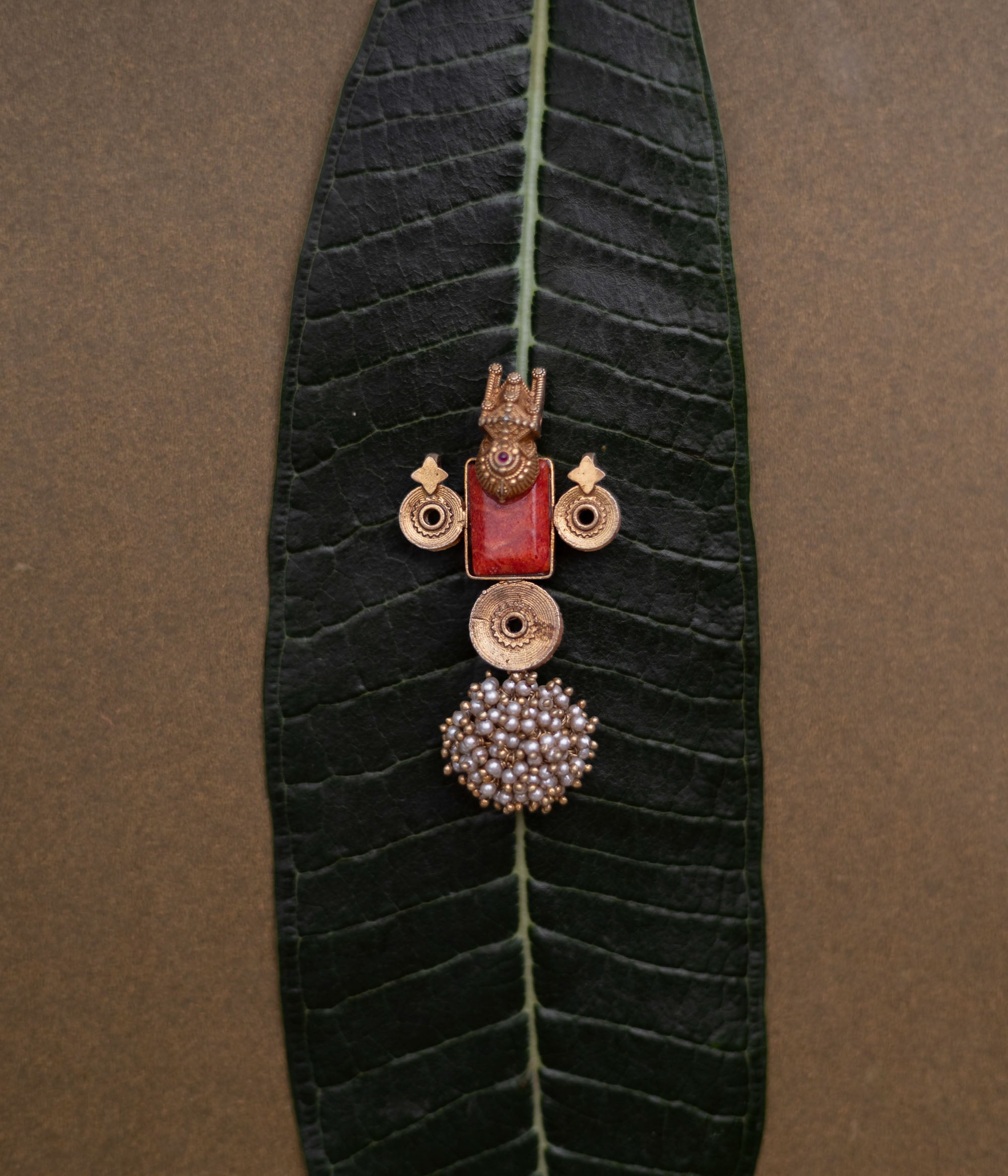 Temple-style pendant with red stone, deity motif, antique gold finish, and pearl cluster base.