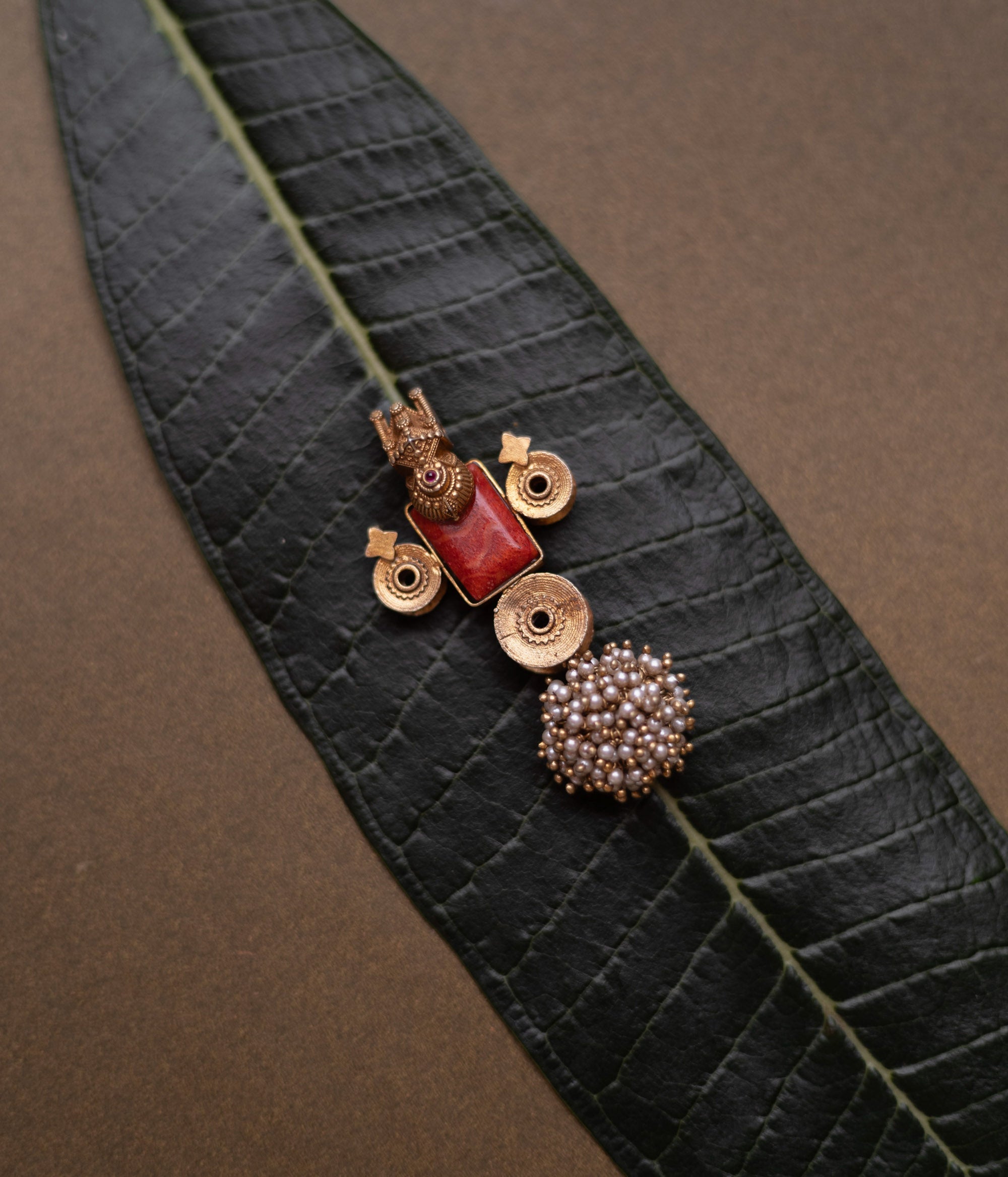 Temple-style pendant with red stone, deity motif, antique gold finish, and pearl cluster base.