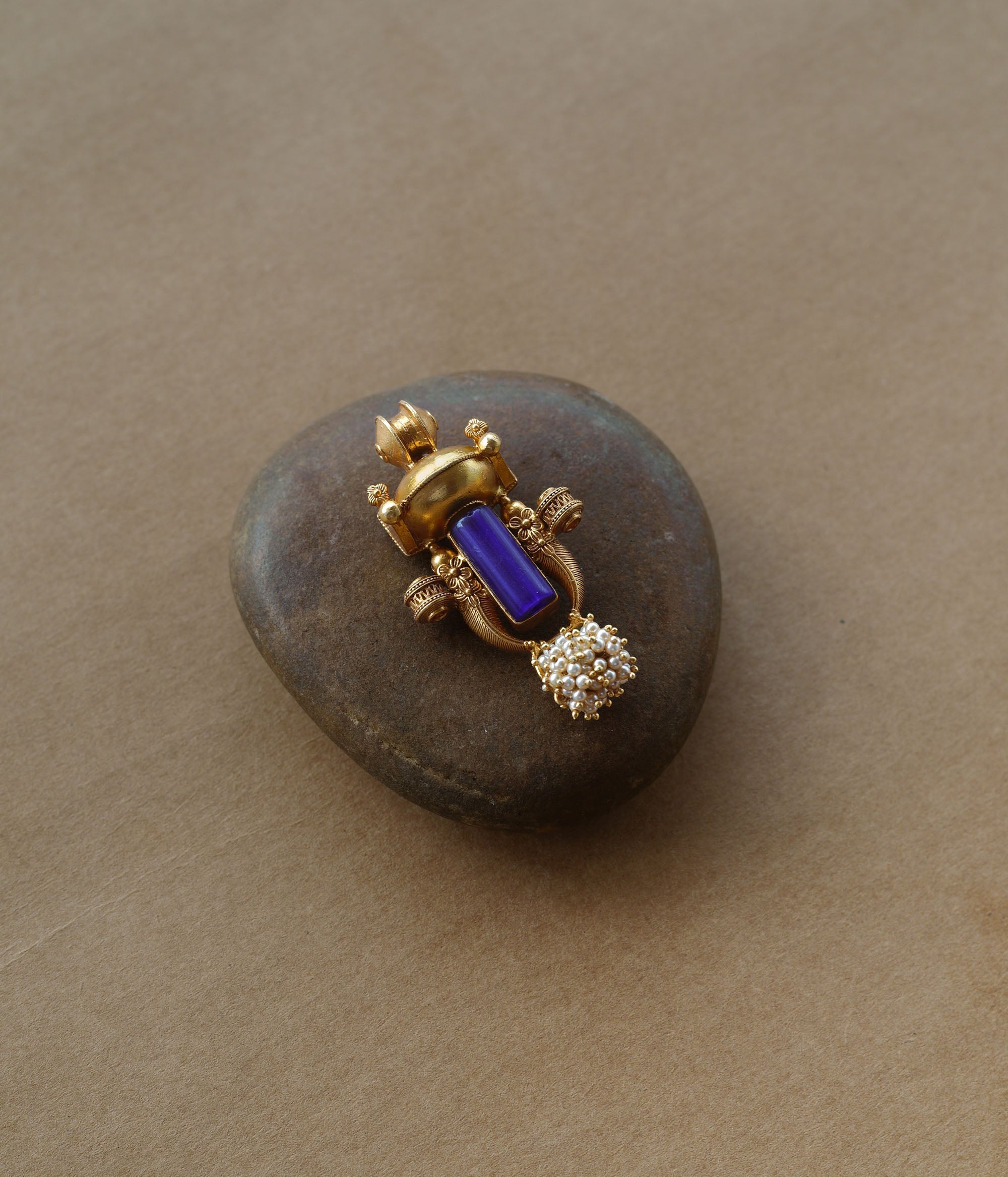 Gold tribal pendant with vertical blue stone, pearl cluster, and ornate sacred motifs.