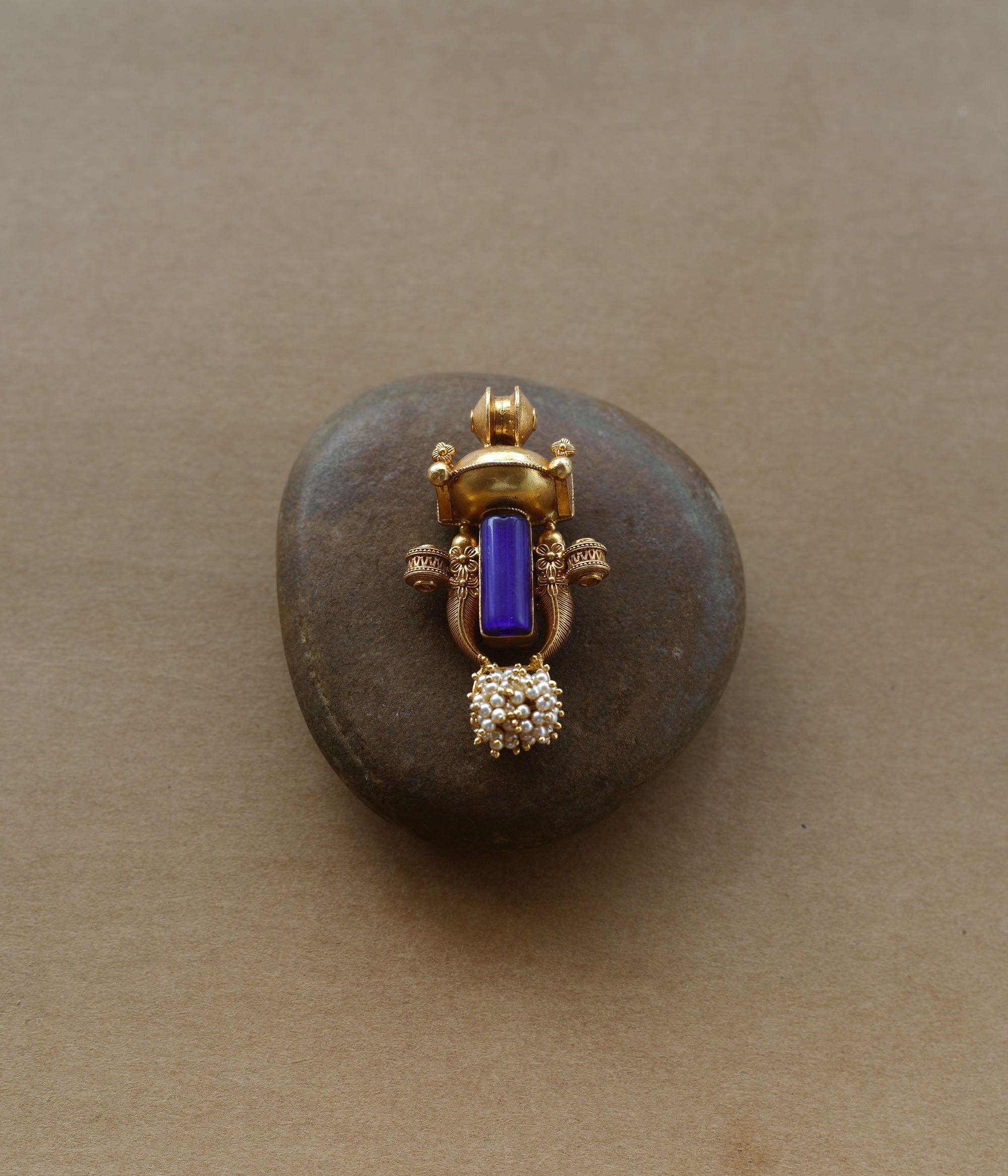 Gold tribal pendant with vertical blue stone, pearl cluster, and ornate sacred motifs.