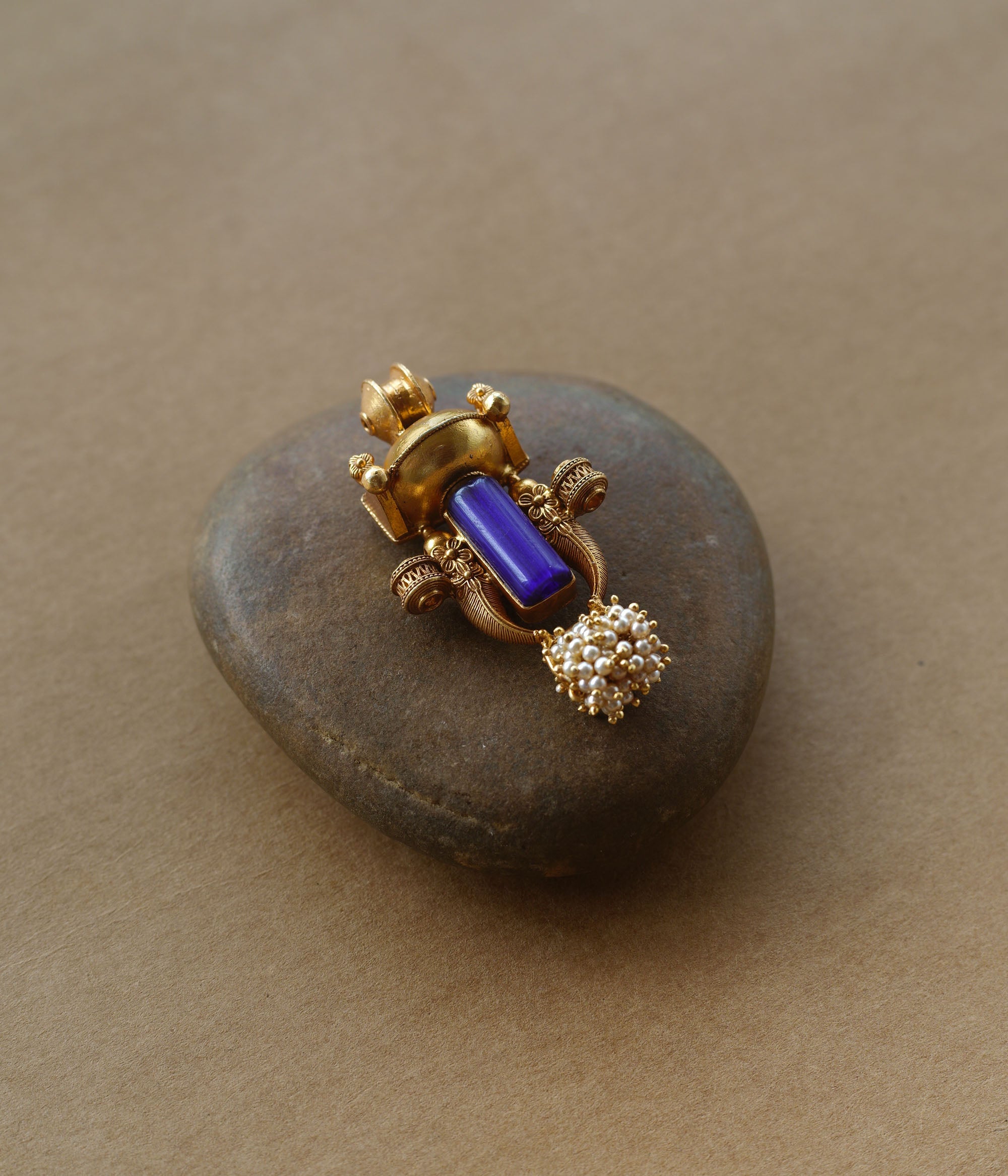 Gold tribal pendant with vertical blue stone, pearl cluster, and ornate sacred motifs.