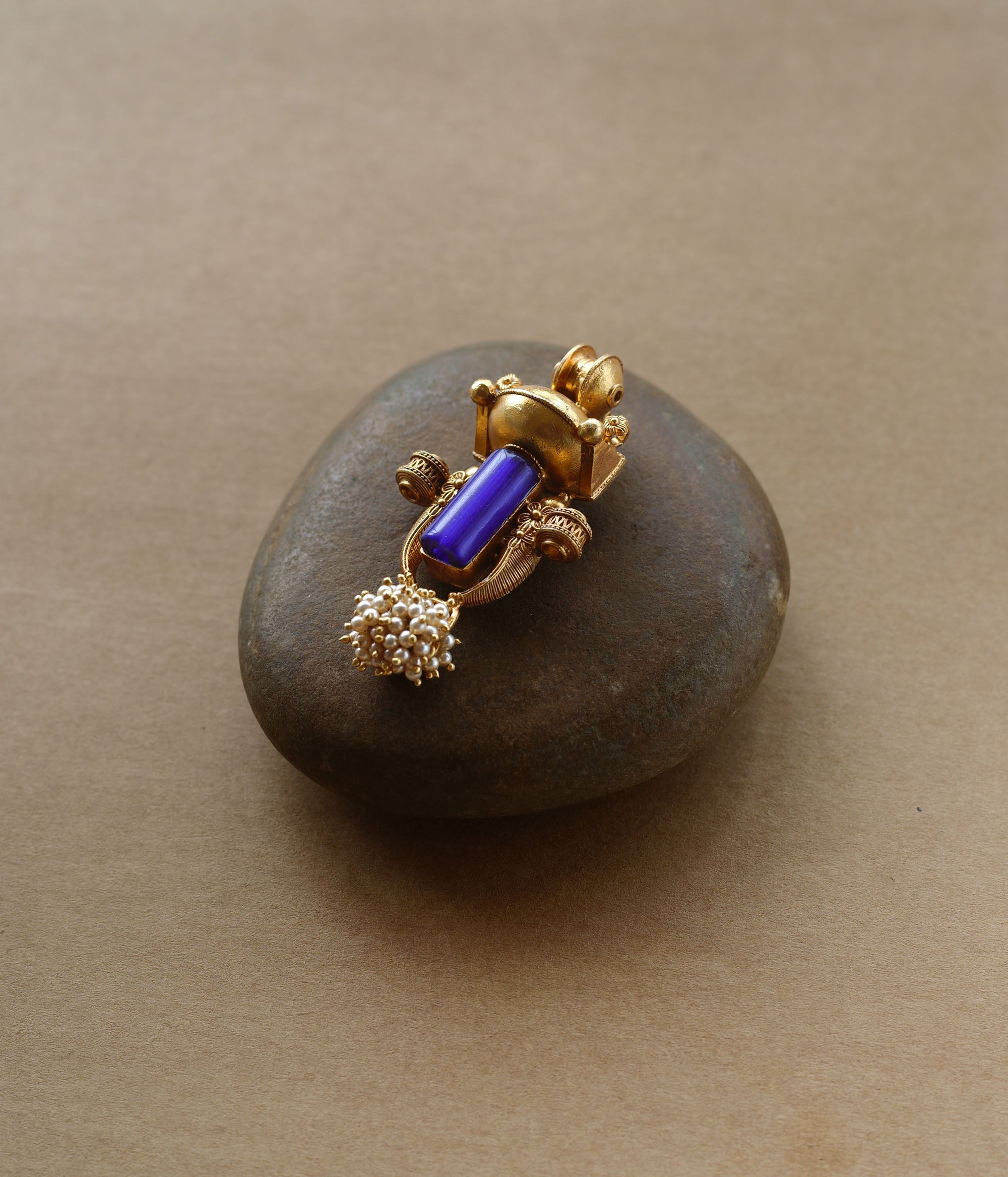 Gold tribal pendant with vertical blue stone, pearl cluster, and ornate sacred motifs.