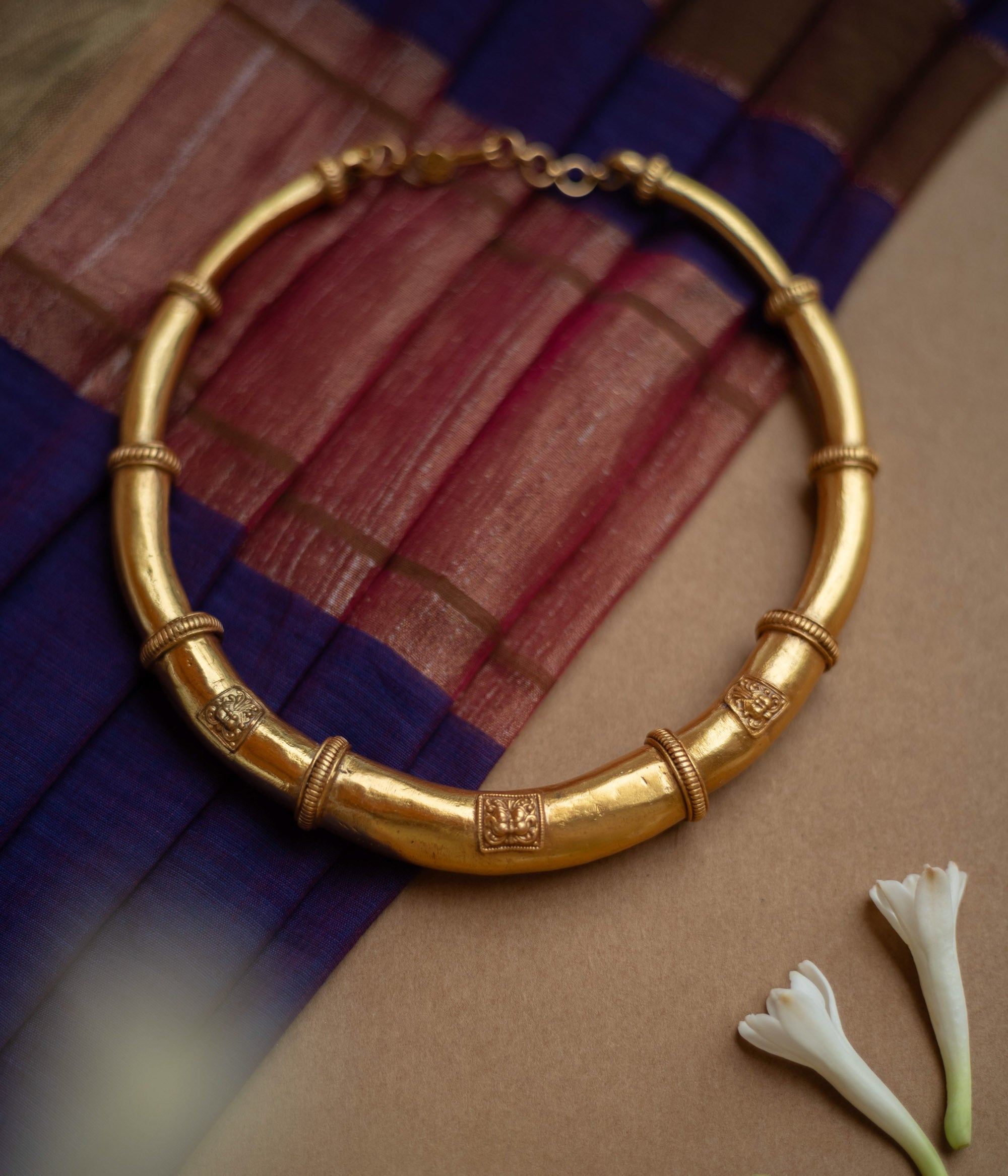 Thick, antique gold hasli necklace with textured bands and square motifs, displayed on fabric.
