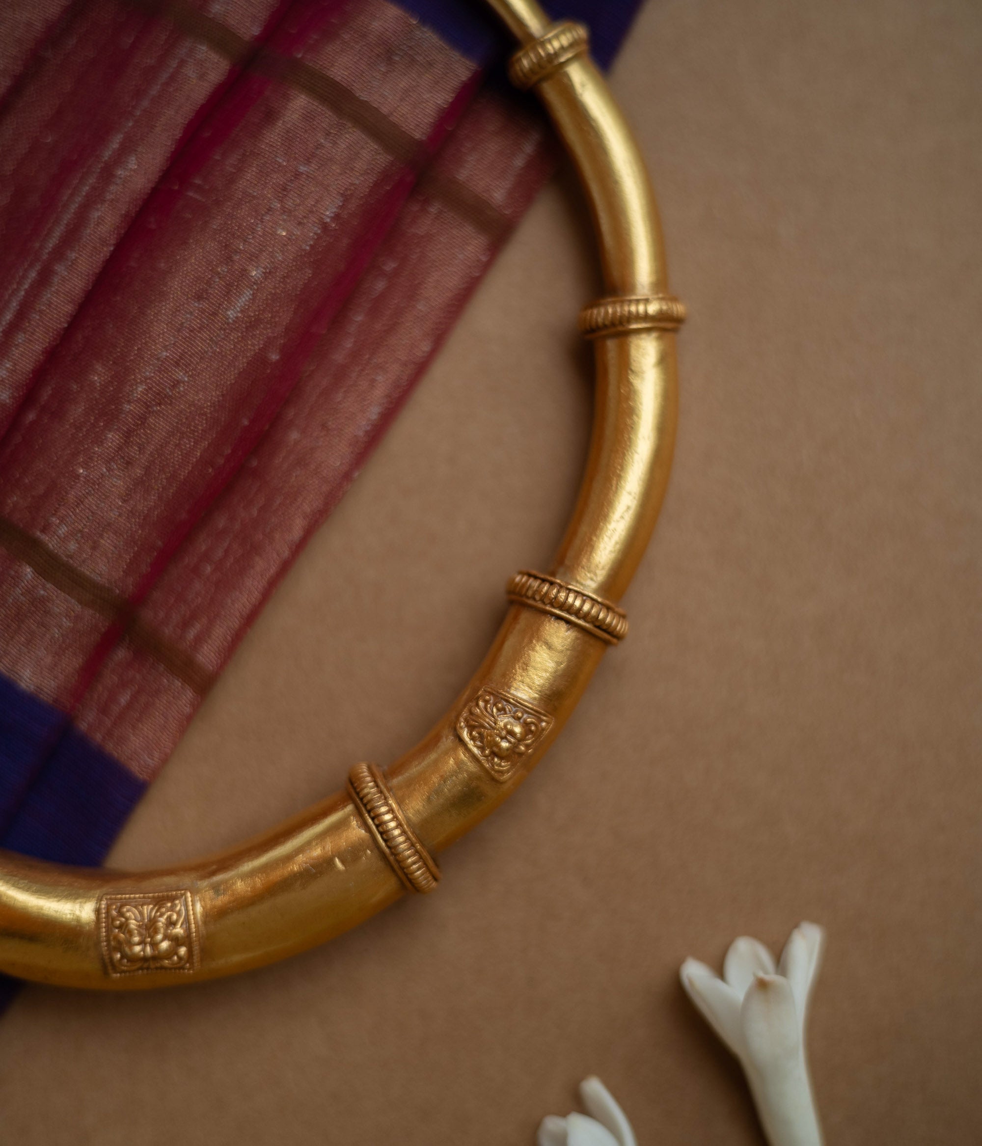 Thick, antique gold hasli necklace with textured bands and square motifs, displayed on fabric.
