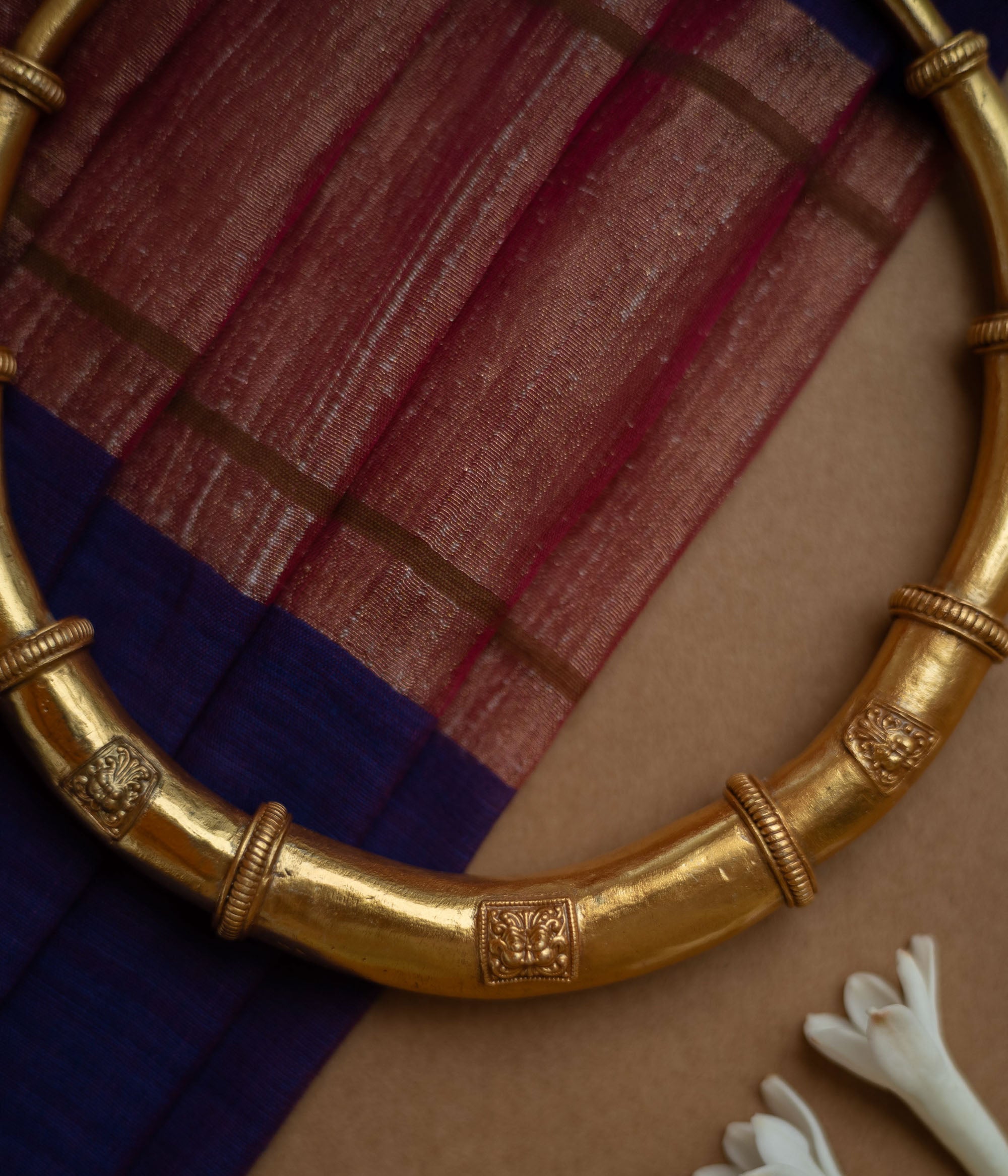 Thick, antique gold hasli necklace with textured bands and square motifs, displayed on fabric.
