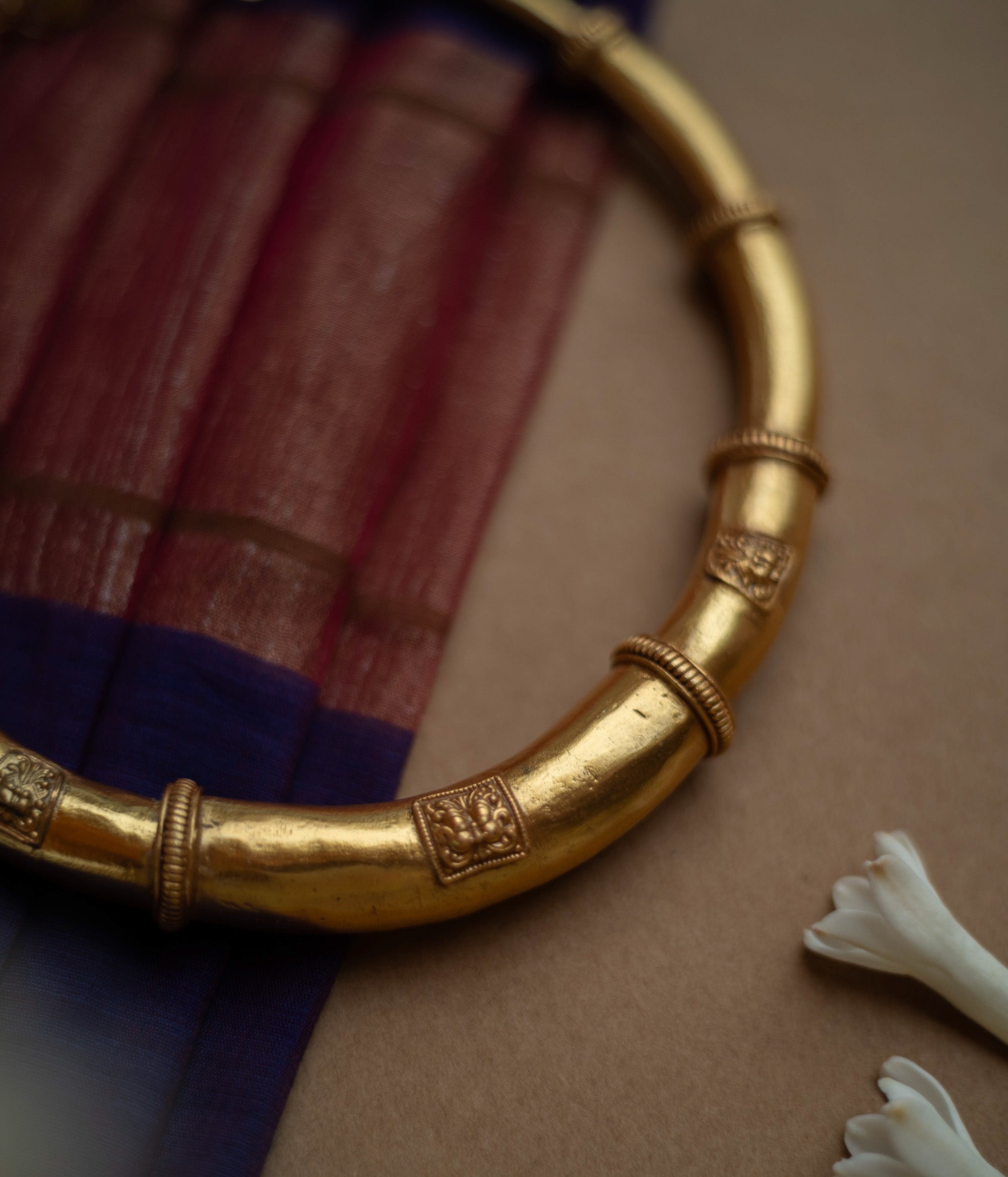 Thick, antique gold hasli necklace with textured bands and square motifs, displayed on fabric.