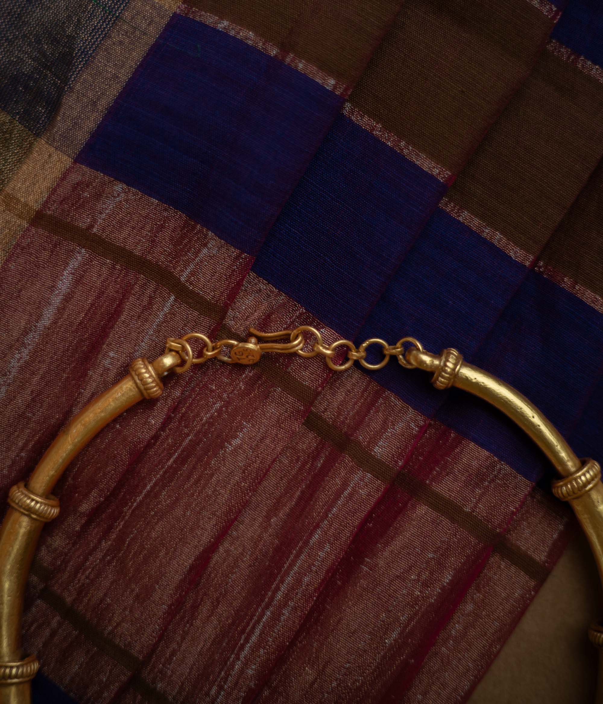 Thick, antique gold hasli necklace with textured bands and square motifs, displayed on fabric.