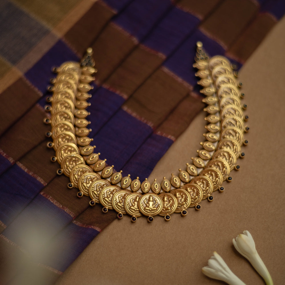 Temple necklace with red stones and goddess coin motifs from Katha Collection on silk fabric.