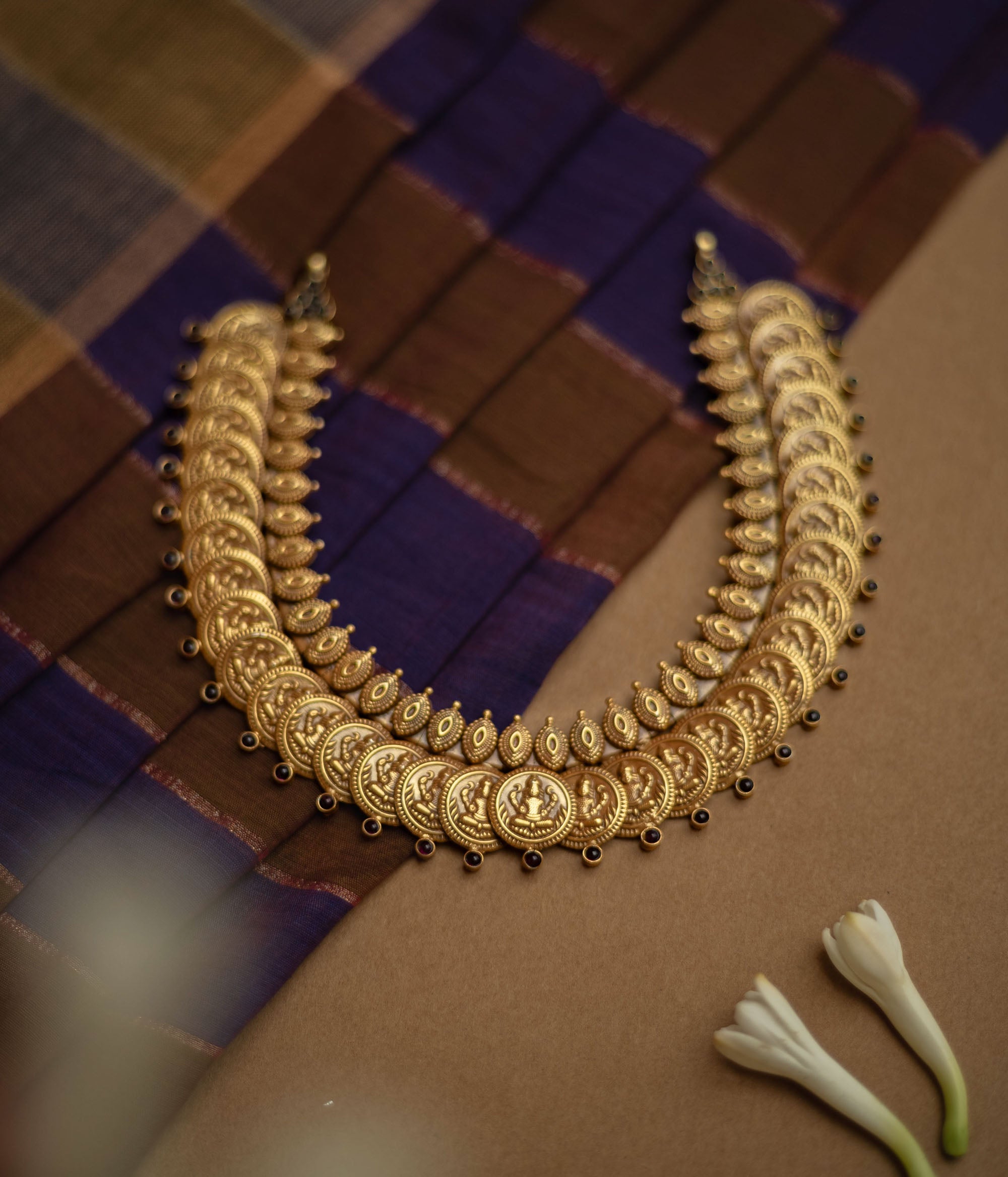 Temple necklace with red stones and goddess coin motifs from Katha Collection on silk fabric.