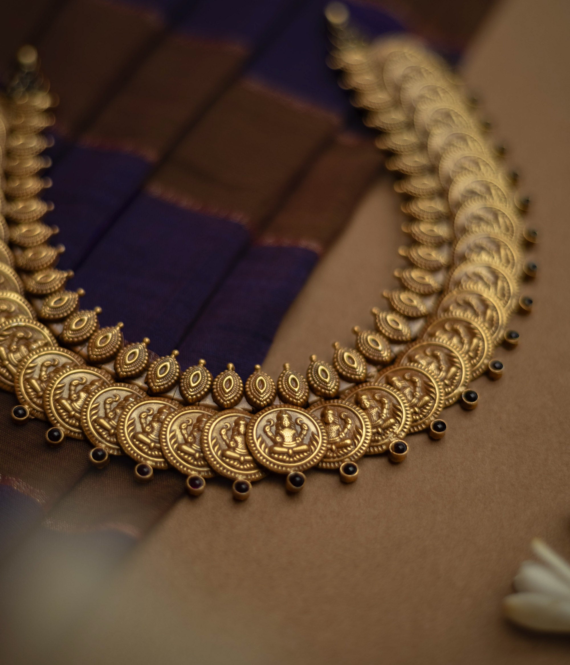 Temple necklace with red stones and goddess coin motifs from Katha Collection on silk fabric.