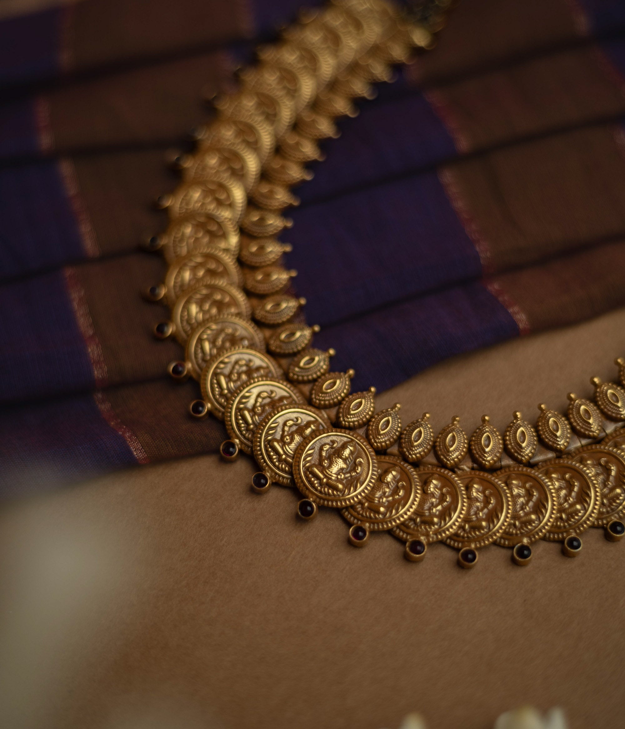 Temple necklace with red stones and goddess coin motifs from Katha Collection on silk fabric.