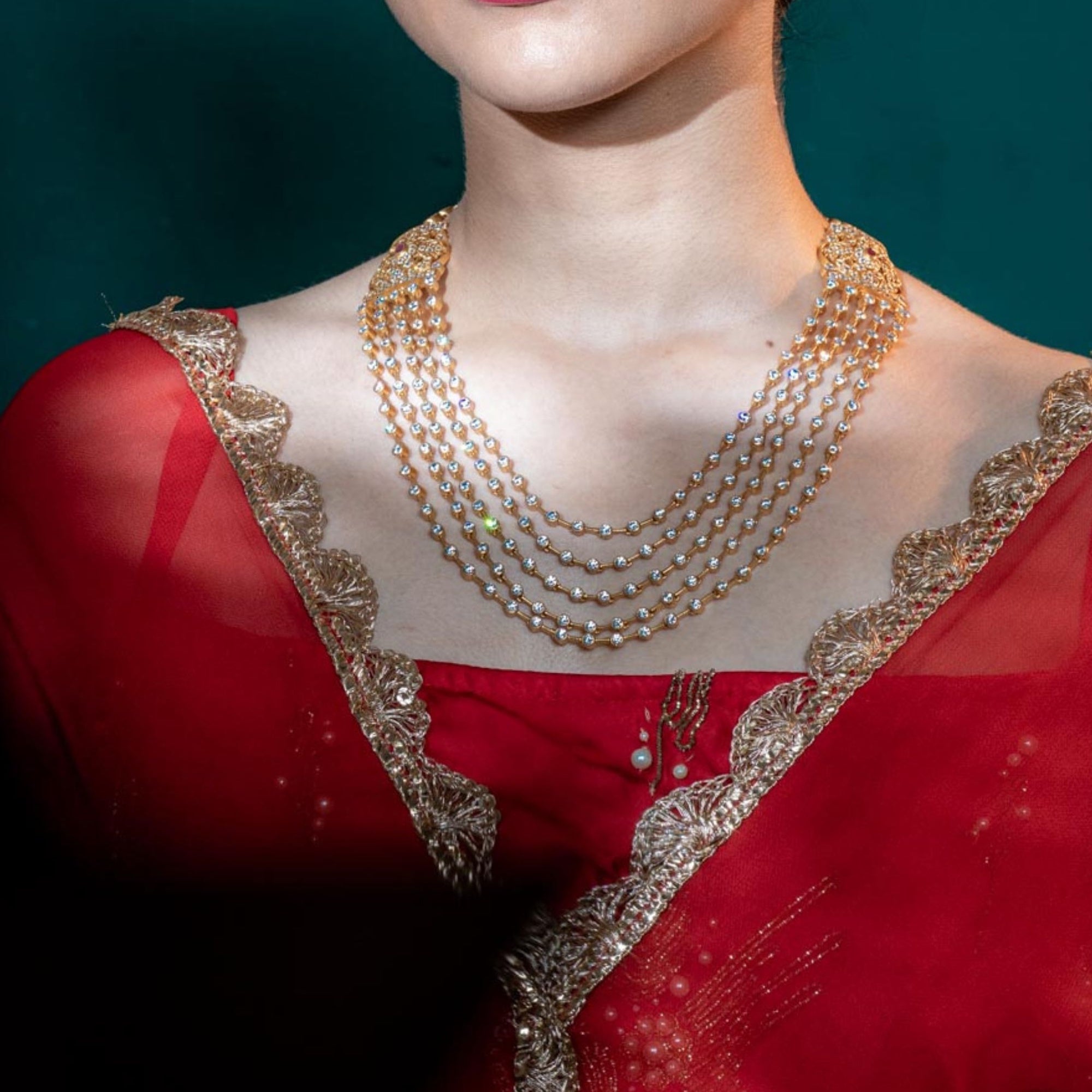 Red garment with gold embroidery and pearl necklace on a mannequin against a dark background