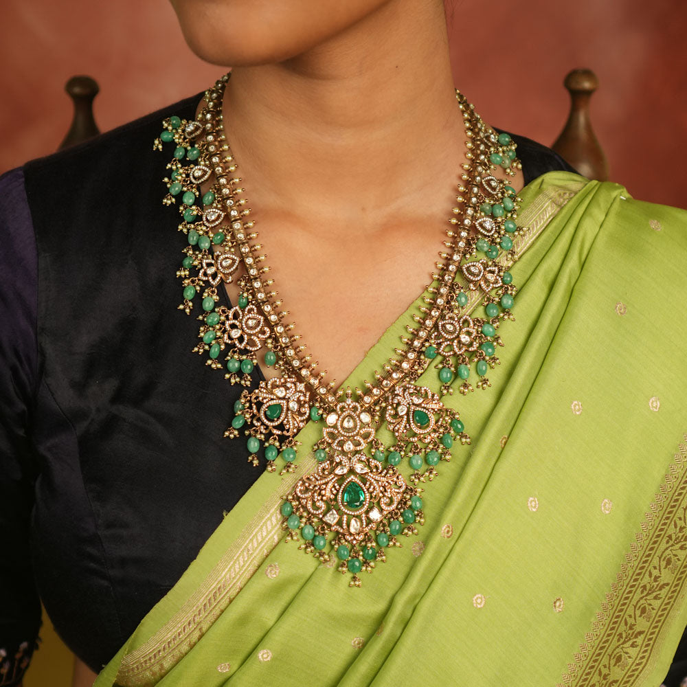 A regal masterpiece adorned with Polki stones, CZ stones, green gemstones, pearls, and delicate green beads, this necklace radiates celestial charm. A timeless creation, shimmering with cosmic grace and exquisite artistry.