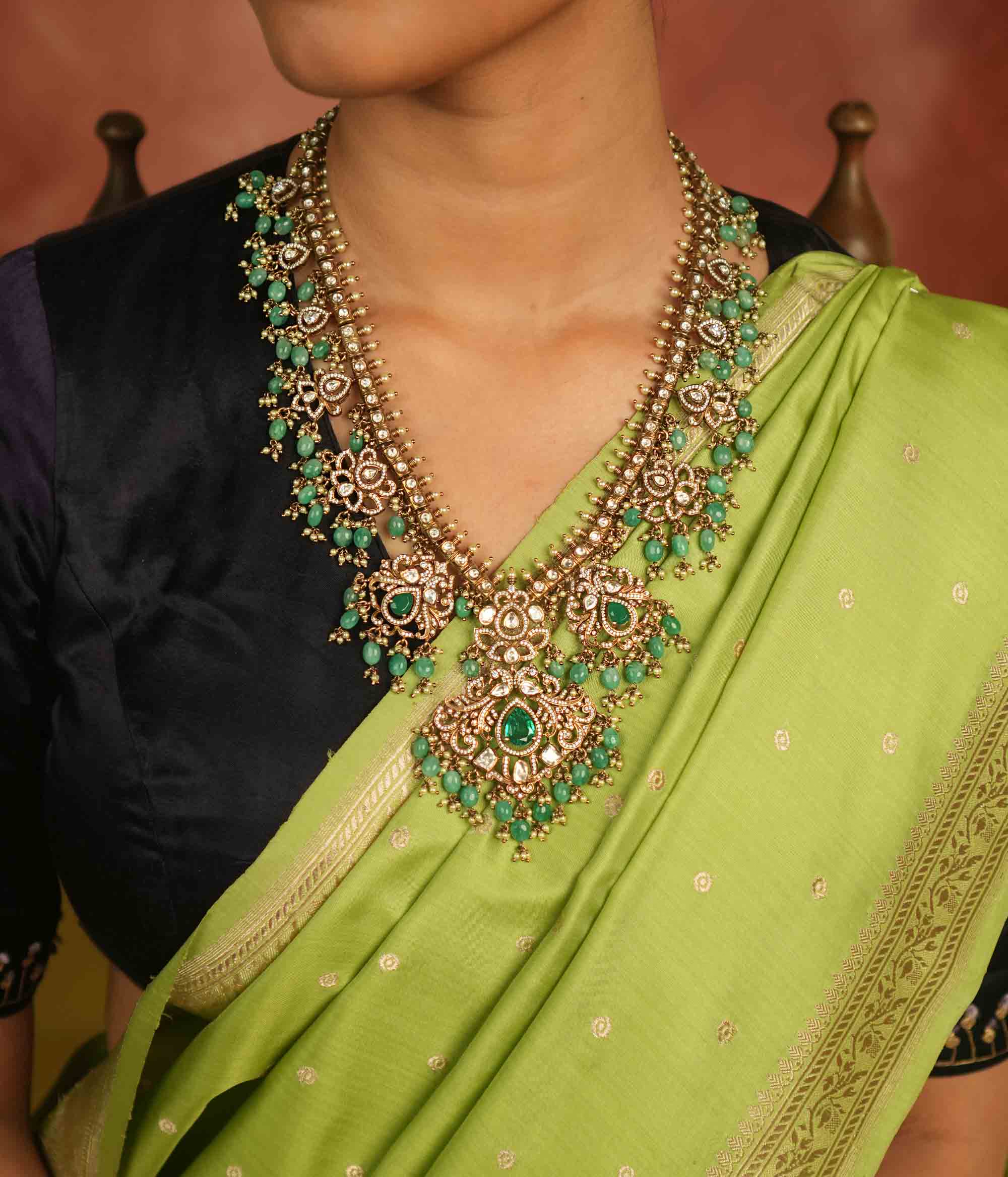 A regal masterpiece adorned with Polki stones, CZ stones, green gemstones, pearls, and delicate green beads, this necklace radiates celestial charm. A timeless creation, shimmering with cosmic grace and exquisite artistry.