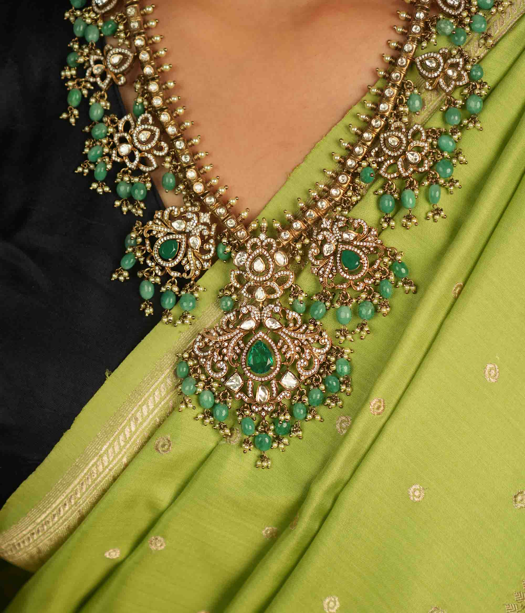 A regal masterpiece adorned with Polki stones, CZ stones, green gemstones, pearls, and delicate green beads, this necklace radiates celestial charm. A timeless creation, shimmering with cosmic grace and exquisite artistry.