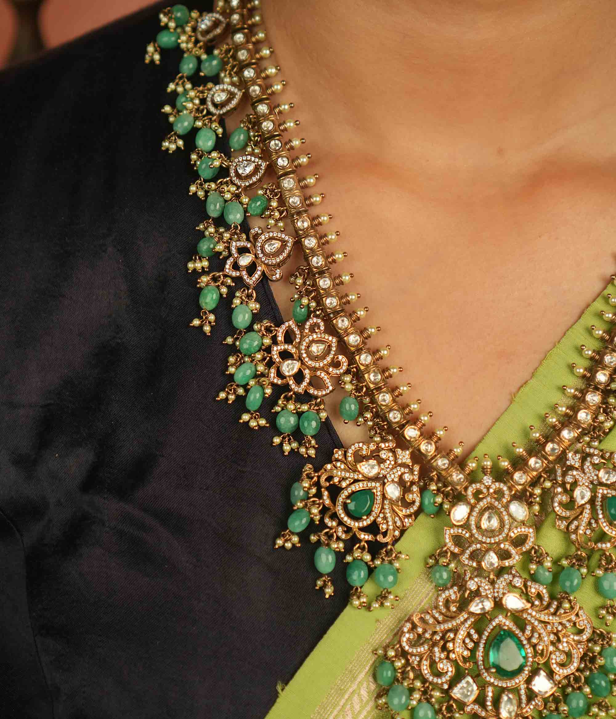 A regal masterpiece adorned with Polki stones, CZ stones, green gemstones, pearls, and delicate green beads, this necklace radiates celestial charm. A timeless creation, shimmering with cosmic grace and exquisite artistry.