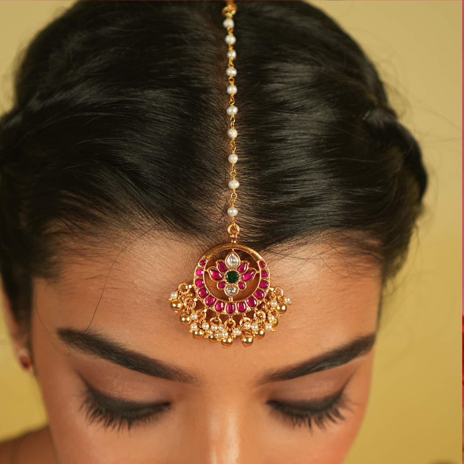 The Tavleen Kundan Tikka showcases a stunning combination of red, green, and white Kundan stones, beautifully accented with elegant pearls. This piece exudes a timeless, regal charm, making it a perfect addition to any collection.