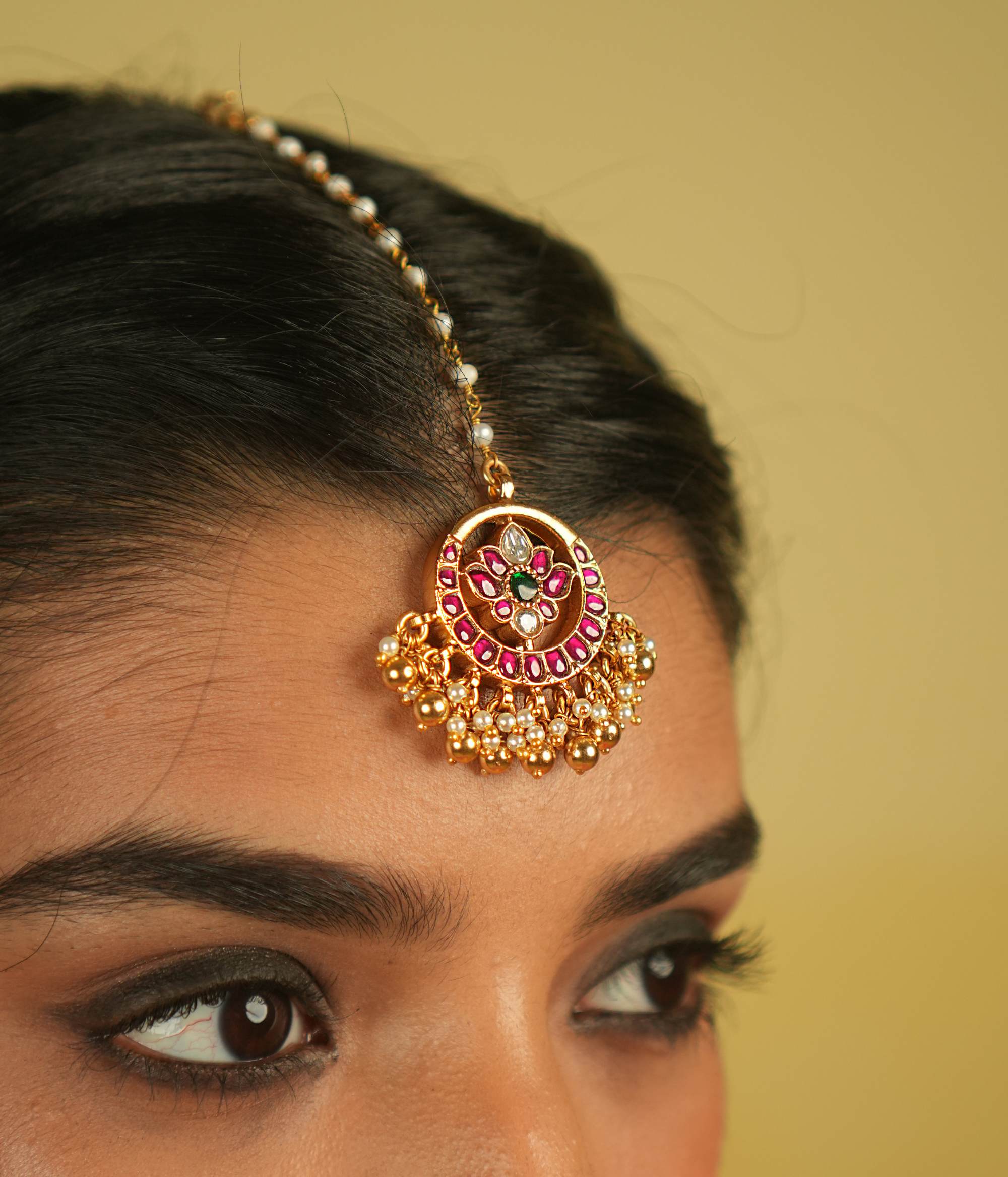 The Tavleen Kundan Tikka showcases a stunning combination of red, green, and white Kundan stones, beautifully accented with elegant pearls. This piece exudes a timeless, regal charm, making it a perfect addition to any collection.