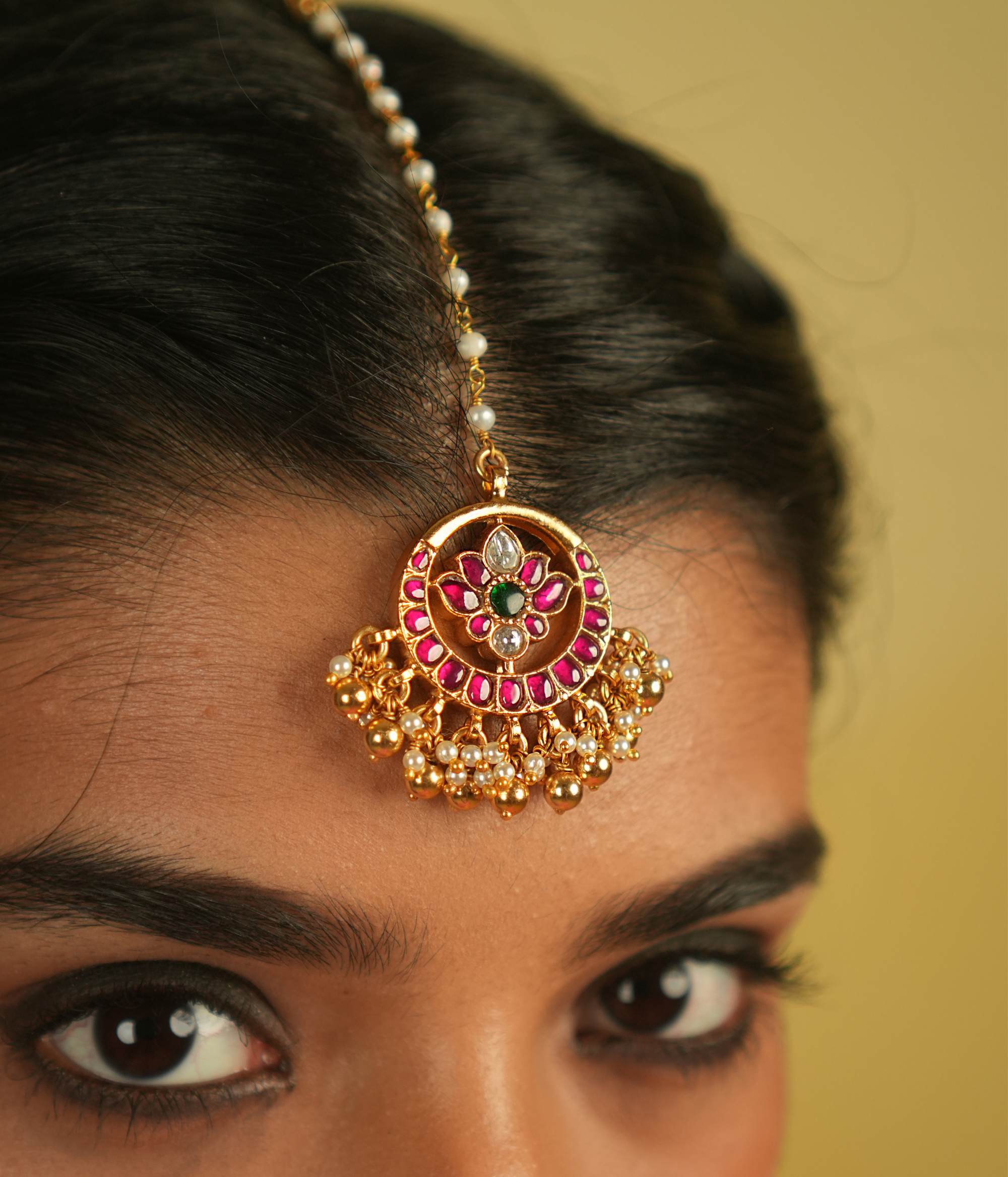 The Tavleen Kundan Tikka showcases a stunning combination of red, green, and white Kundan stones, beautifully accented with elegant pearls. This piece exudes a timeless, regal charm, making it a perfect addition to any collection.