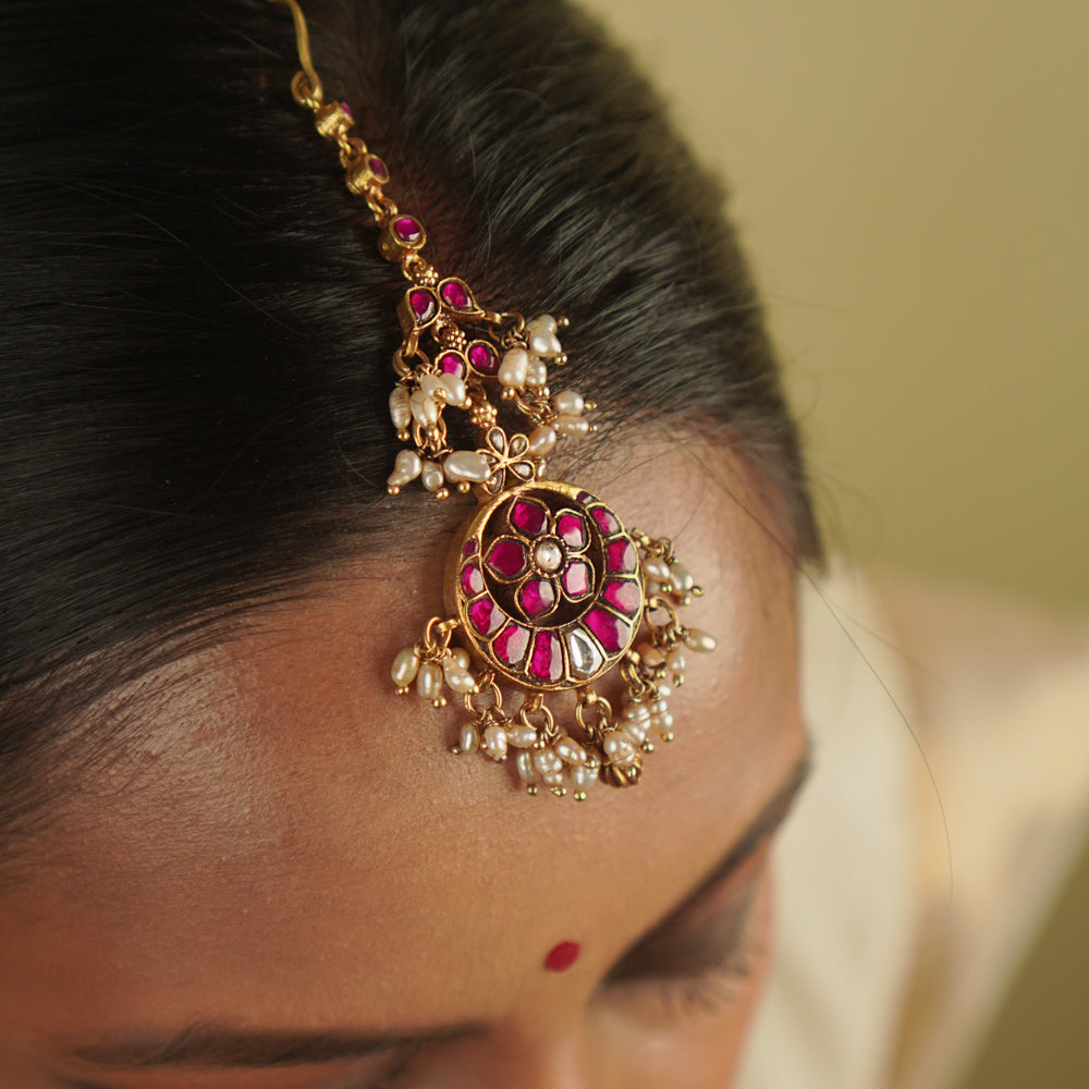 Toral Maangtika: A redefinition of regal elegance. Crafted in gold-plated silver, this exquisite tikka features red kundan stones and white pearls, forming a dazzling design. Fit for royalty, it’s a statement of timeless beauty.