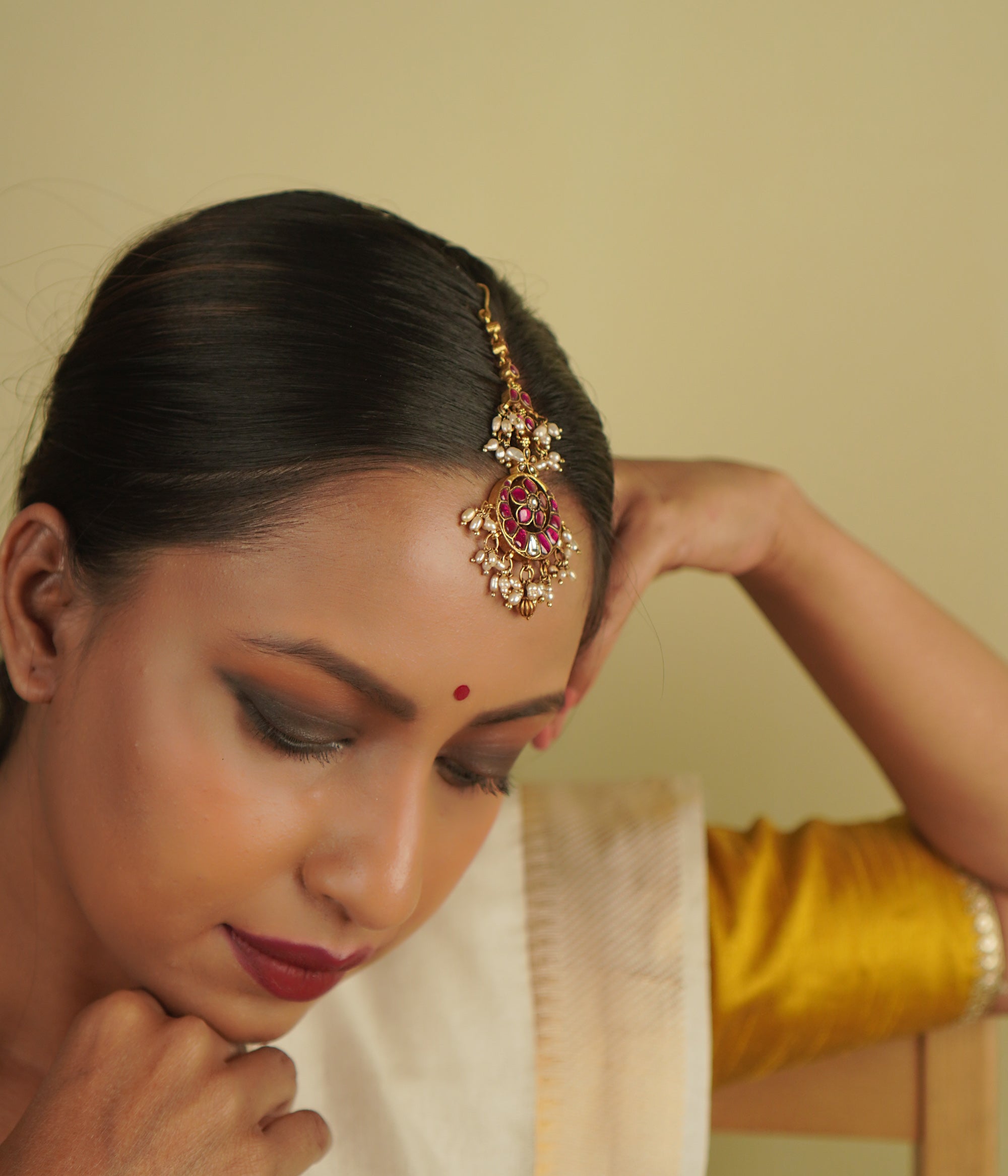 Toral Maangtika: A redefinition of regal elegance. Crafted in gold-plated silver, this exquisite tikka features red kundan stones and white pearls, forming a dazzling design. Fit for royalty, it’s a statement of timeless beauty.