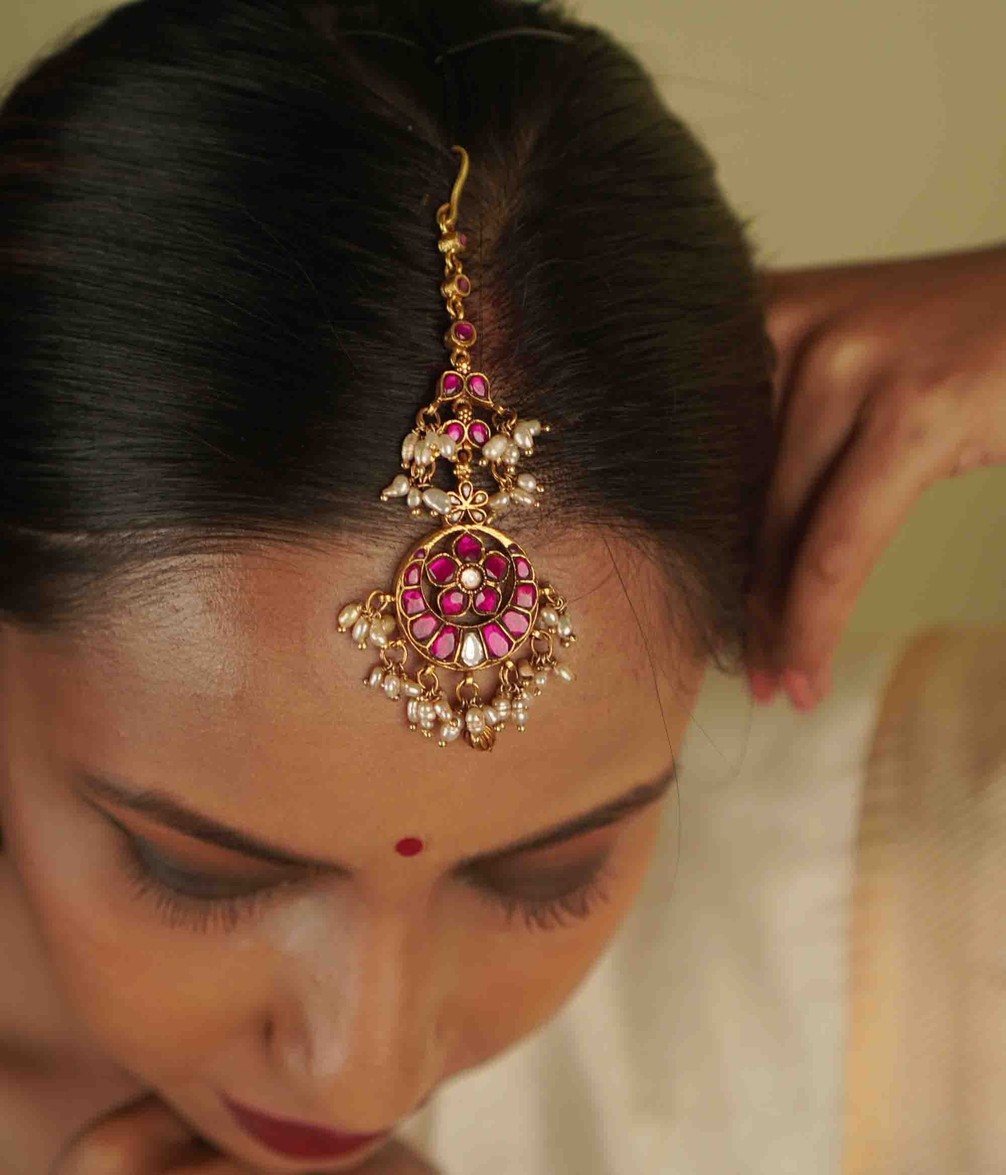 Toral Maangtika: A redefinition of regal elegance. Crafted in gold-plated silver, this exquisite tikka features red kundan stones and white pearls, forming a dazzling design. Fit for royalty, it’s a statement of timeless beauty.