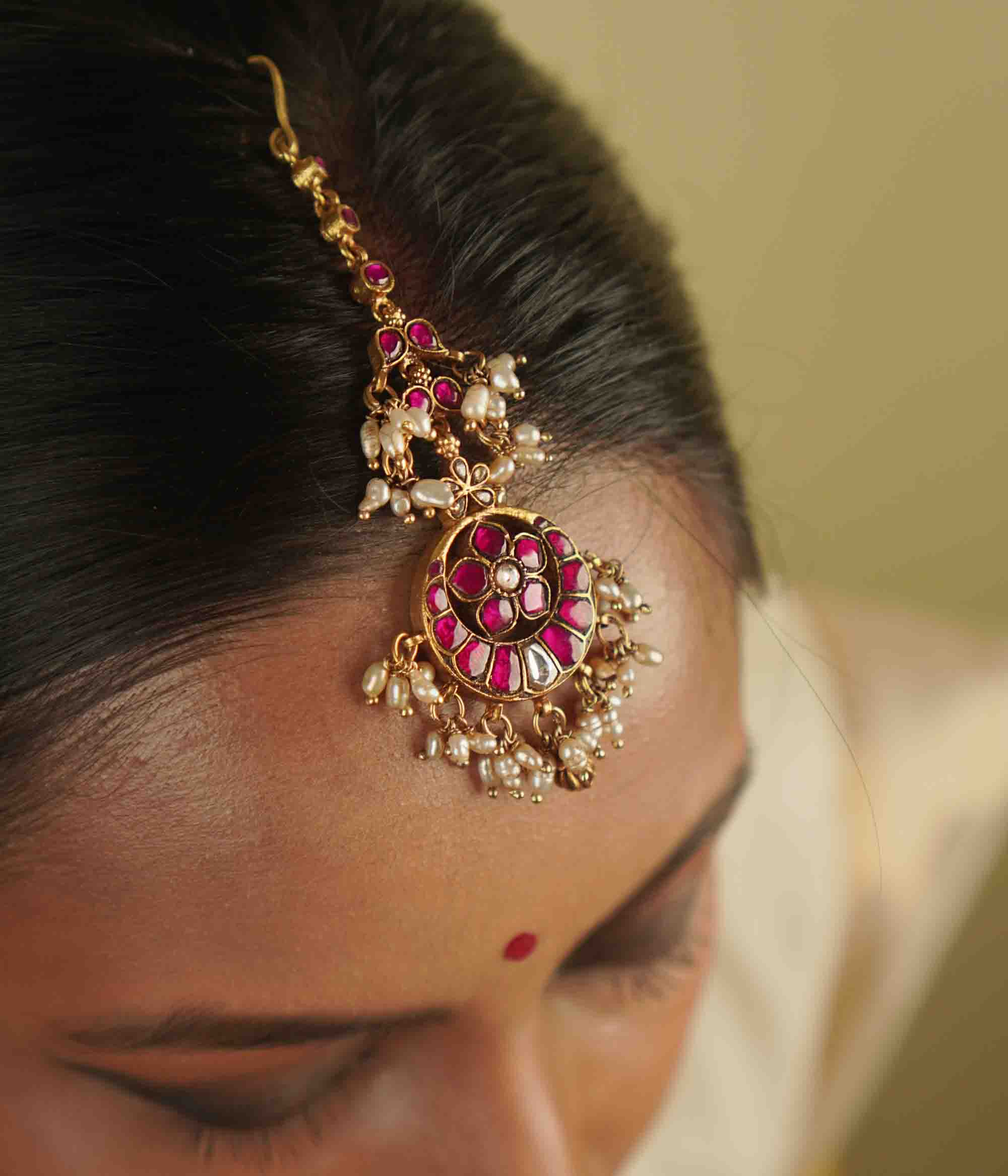 Toral Maangtika: A redefinition of regal elegance. Crafted in gold-plated silver, this exquisite tikka features red kundan stones and white pearls, forming a dazzling design. Fit for royalty, it’s a statement of timeless beauty.