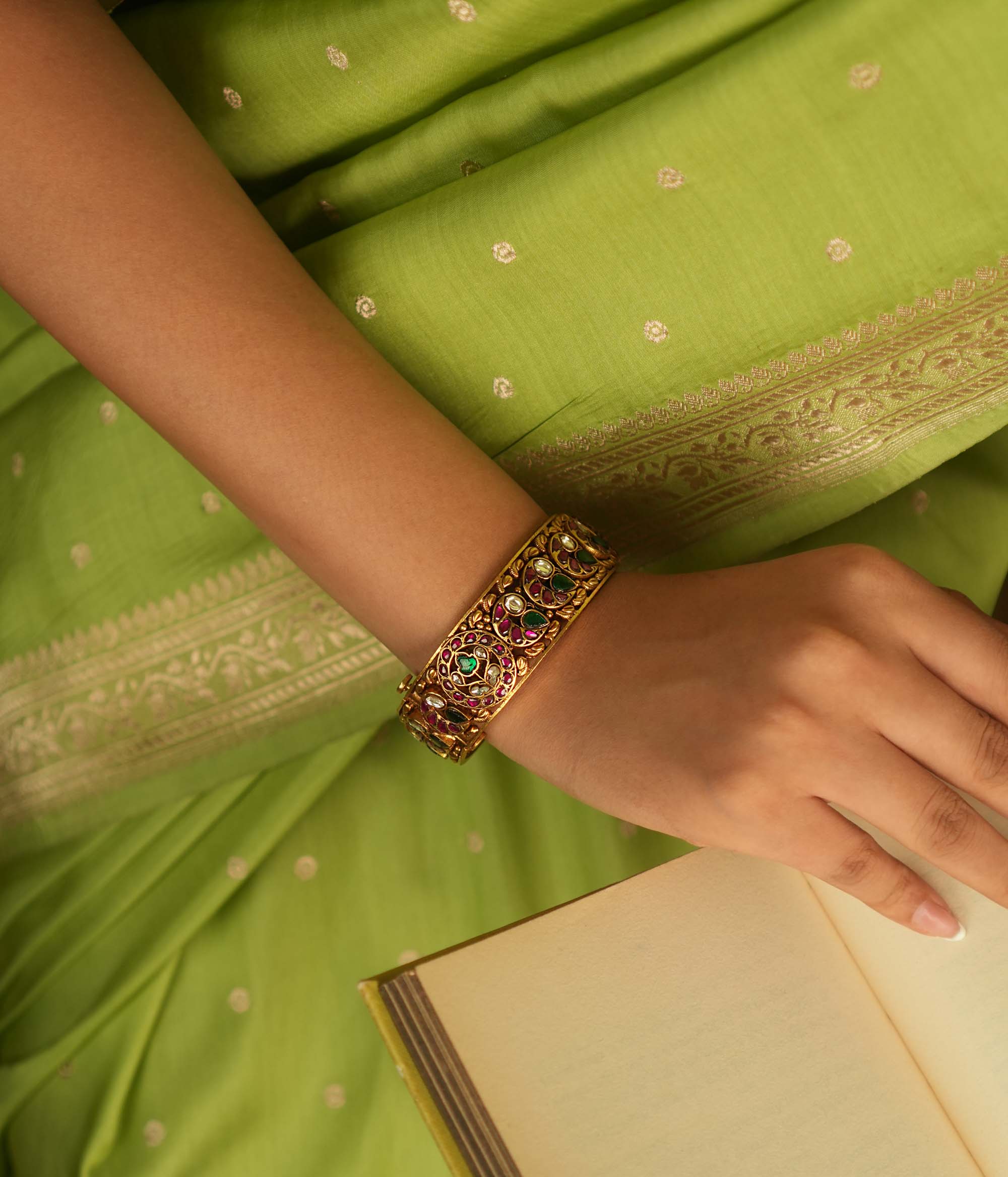 A stunning bangle featuring a peacock motif, adorned with red, white, and green Kundan stones. The vibrant hues of the Kundan stones gleam, embodying royal opulence. A masterpiece of intricate craftsmanship, this bangle exudes timeless allure.