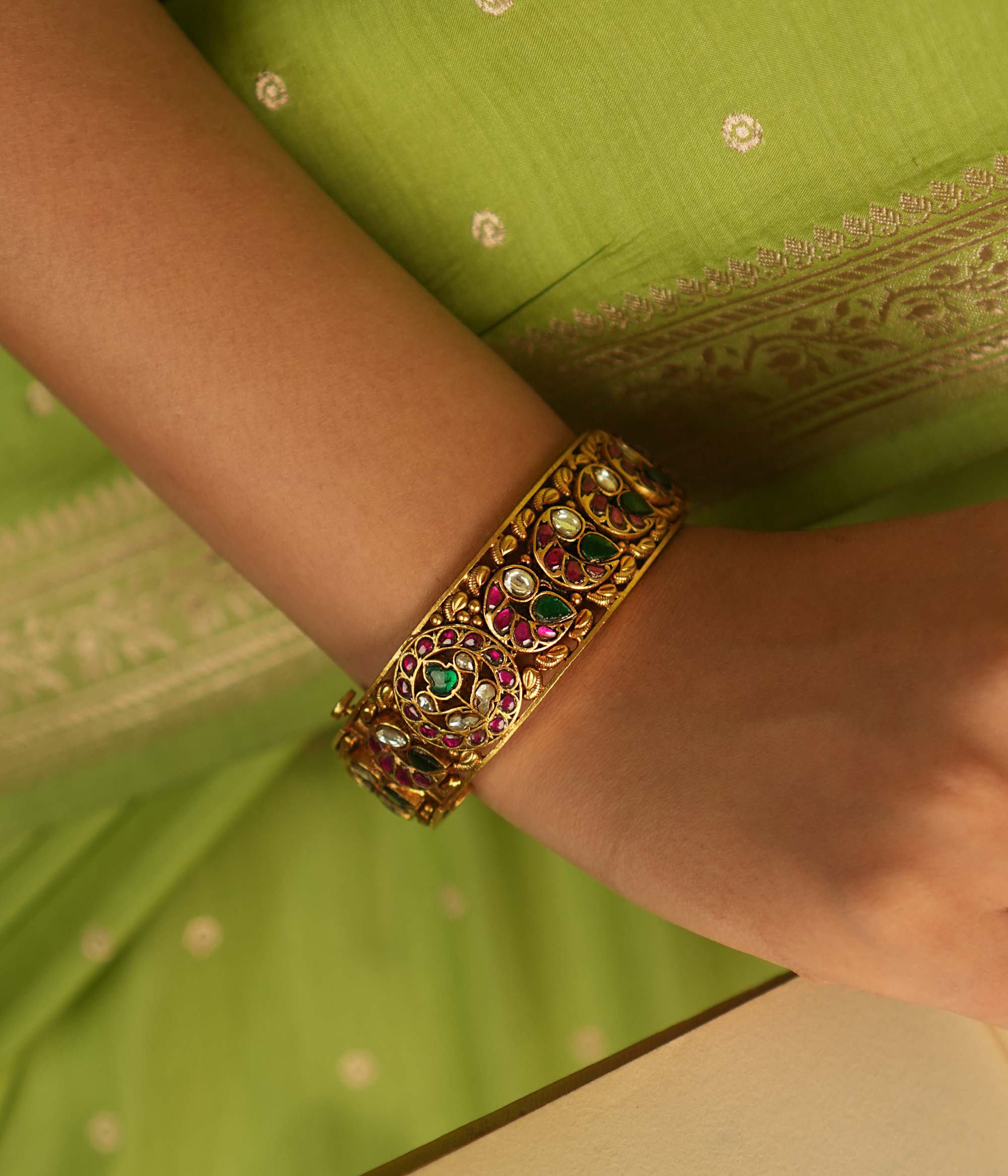 A stunning bangle featuring a peacock motif, adorned with red, white, and green Kundan stones. The vibrant hues of the Kundan stones gleam, embodying royal opulence. A masterpiece of intricate craftsmanship, this bangle exudes timeless allure.