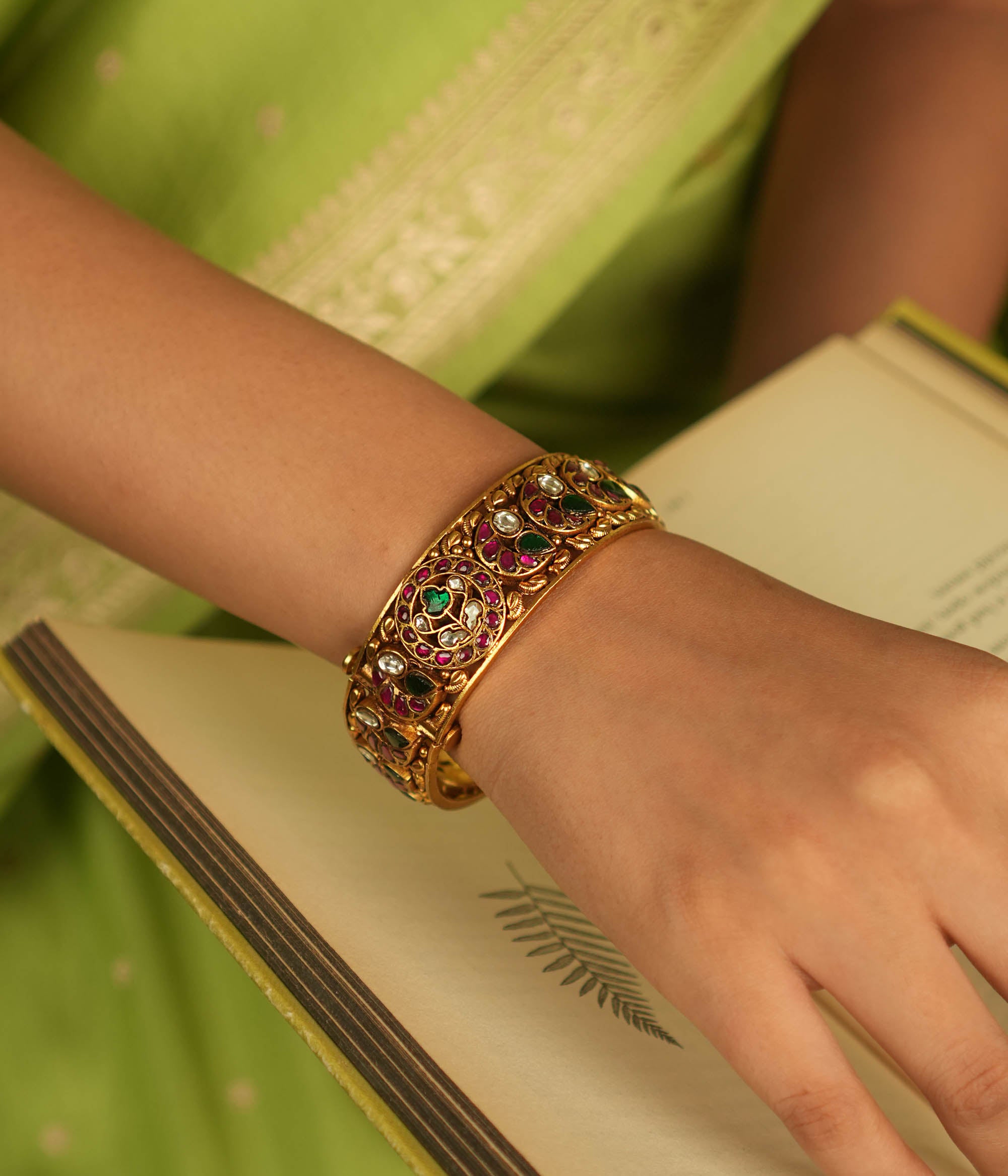 A stunning bangle featuring a peacock motif, adorned with red, white, and green Kundan stones. The vibrant hues of the Kundan stones gleam, embodying royal opulence. A masterpiece of intricate craftsmanship, this bangle exudes timeless allure.