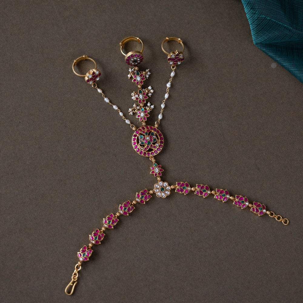 Handmade 92.5 sterling silver and 22ct gold-plated Trishika Haathphool, adorned with white, red, and green Kundan stones and pearls. An intricate masterpiece of elegance and tradition, weaving royal charm with delicate floral accents.