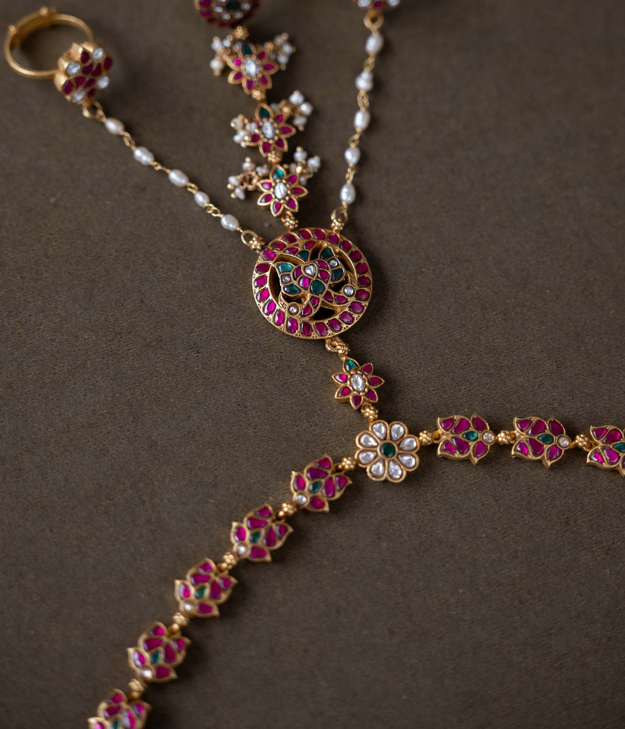 Handmade 92.5 sterling silver and 22ct gold-plated Trishika Haathphool, adorned with white, red, and green Kundan stones and pearls. An intricate masterpiece of elegance and tradition, weaving royal charm with delicate floral accents.
