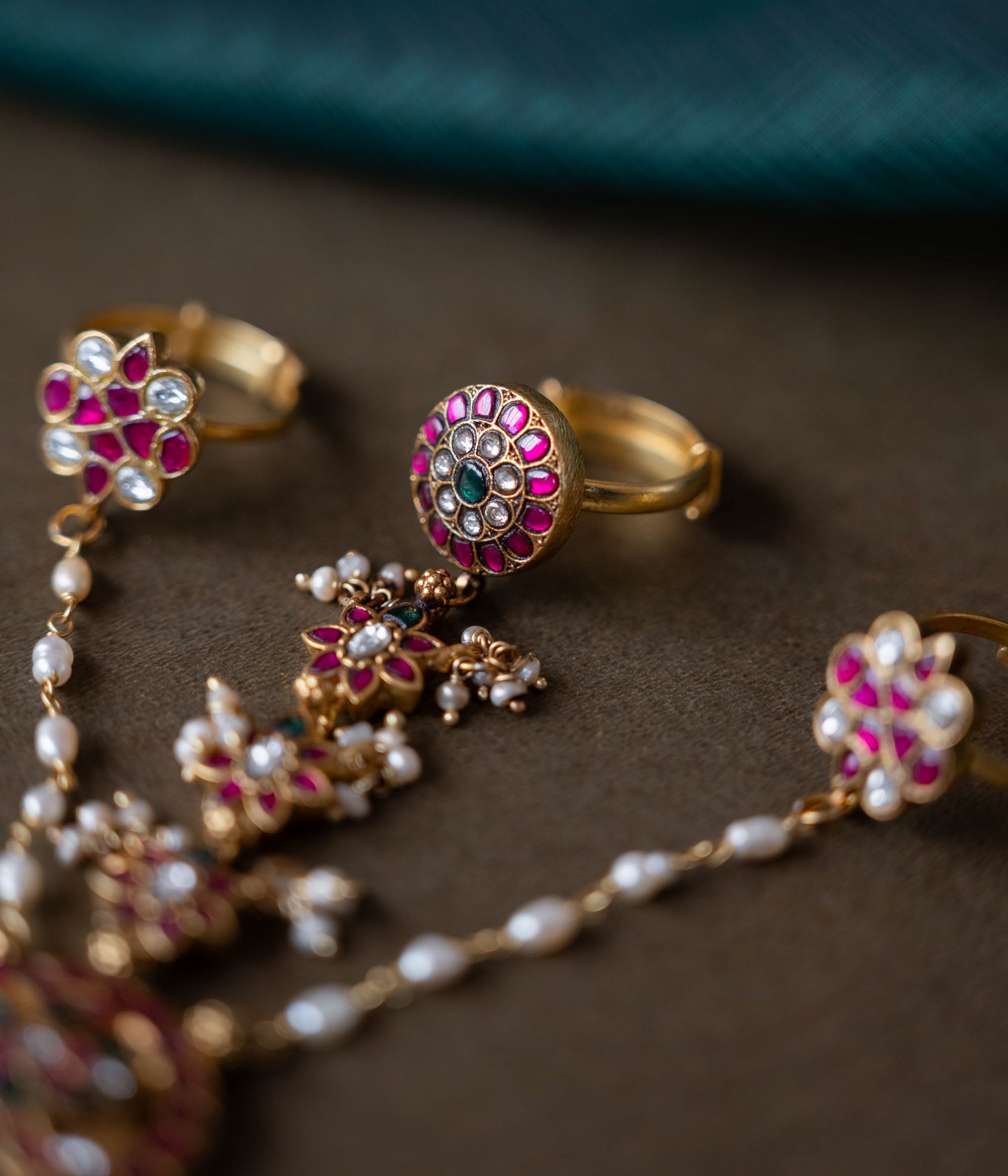Handmade 92.5 sterling silver and 22ct gold-plated Trishika Haathphool, adorned with white, red, and green Kundan stones and pearls. An intricate masterpiece of elegance and tradition, weaving royal charm with delicate floral accents.