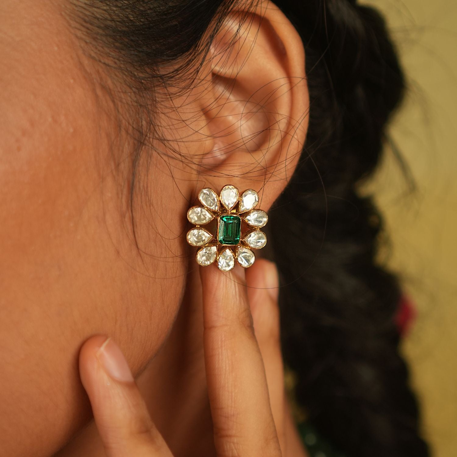 Amidst the vibrant charm of a bustling bazaar, this minimal floral stud with a radiant green cut stone at its heart, encircled by shimmering polki stones, whispers timeless elegance.