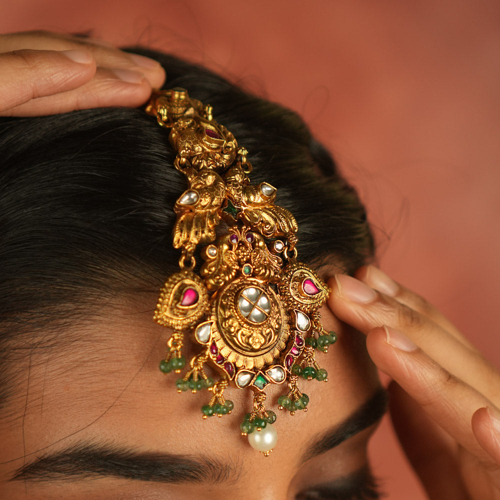 Regal whispers reimagined! A gold-plated maangtika adorned with peacock motifs, vibrant kundan, and delicate pearl droplets—a crown of divine elegance and timeless royalty.