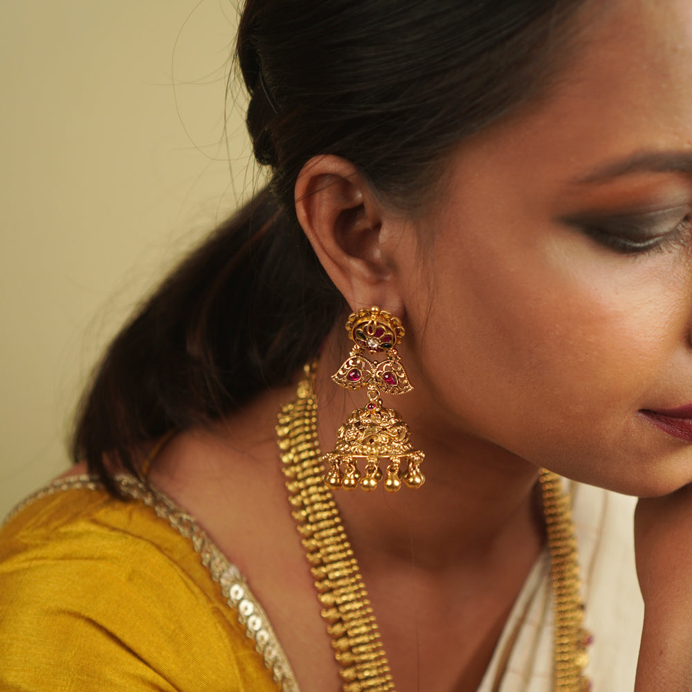 Umika Jhumkas: Echoes of heritage. Antique gold-plated silver with red and green kundans on temple motifs, capturing timeless elegance.
