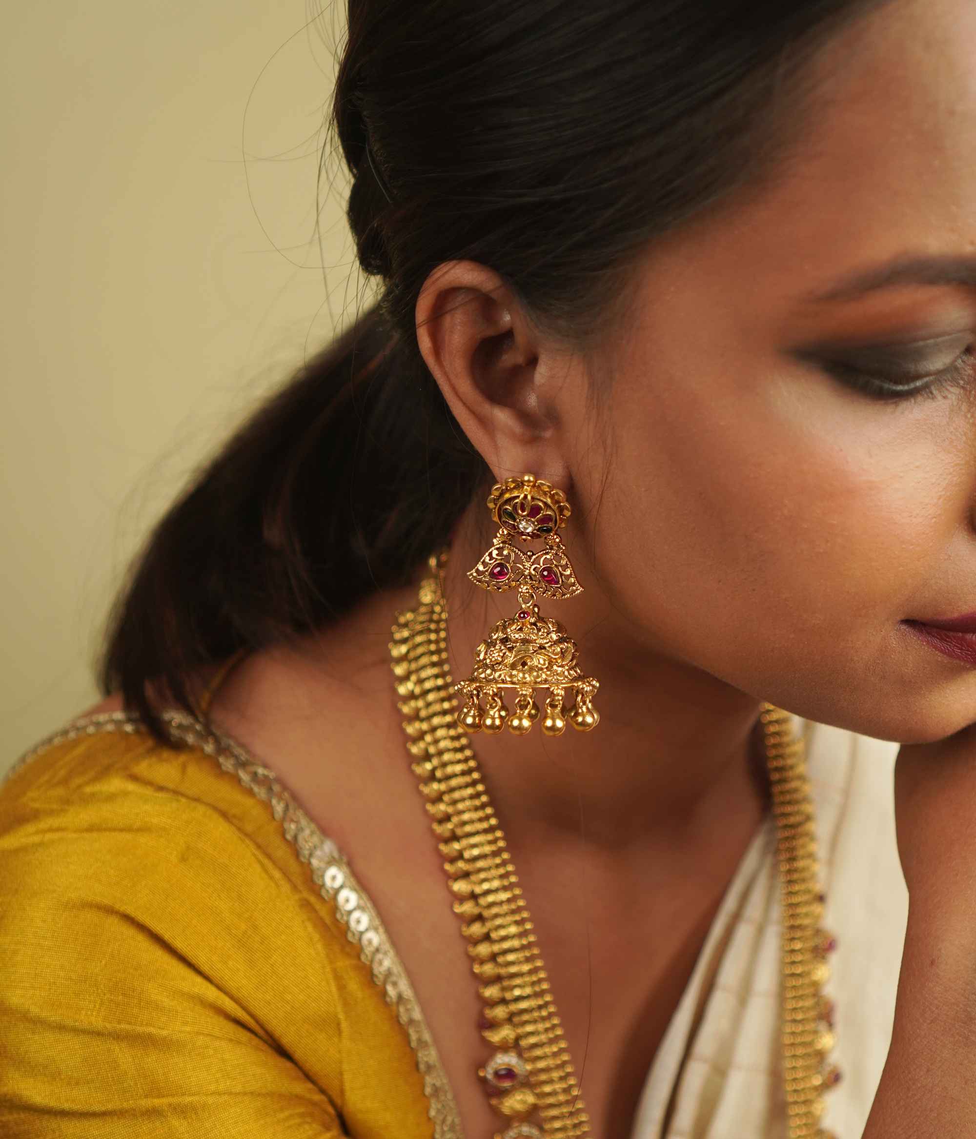 Umika Jhumkas: Echoes of heritage. Antique gold-plated silver with red and green kundans on temple motifs, capturing timeless elegance.