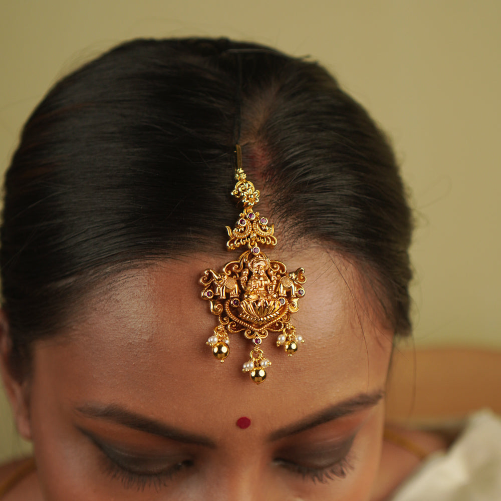 Ura Maangtika: A celebration of vintage charm, reborn. Gold-plated silver adorned with goddess motifs and delicate pearl droplets, blending timeless temple artistry with whimsical elegance, perfect for the modern bride.