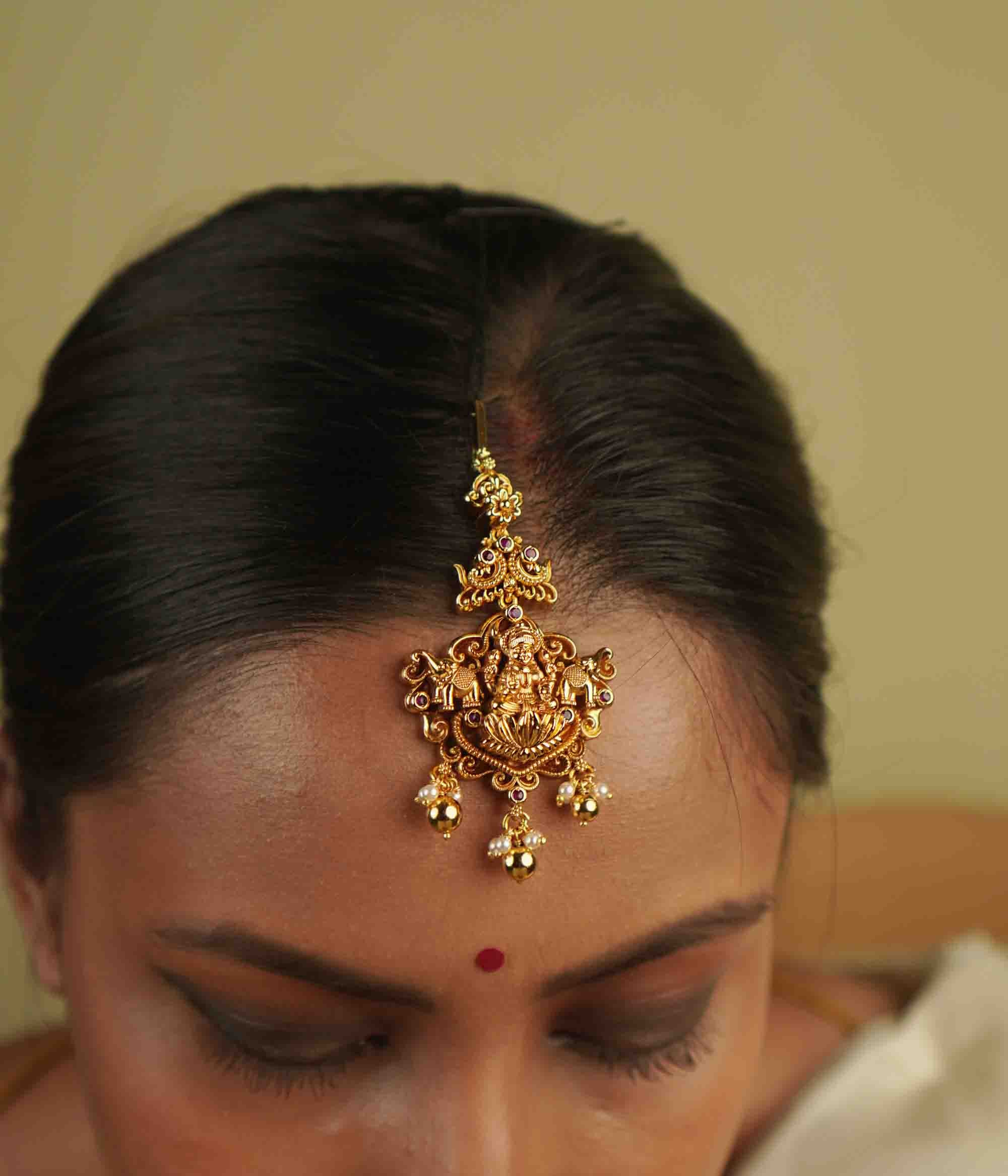 Ura Maangtika: A celebration of vintage charm, reborn. Gold-plated silver adorned with goddess motifs and delicate pearl droplets, blending timeless temple artistry with whimsical elegance, perfect for the modern bride.