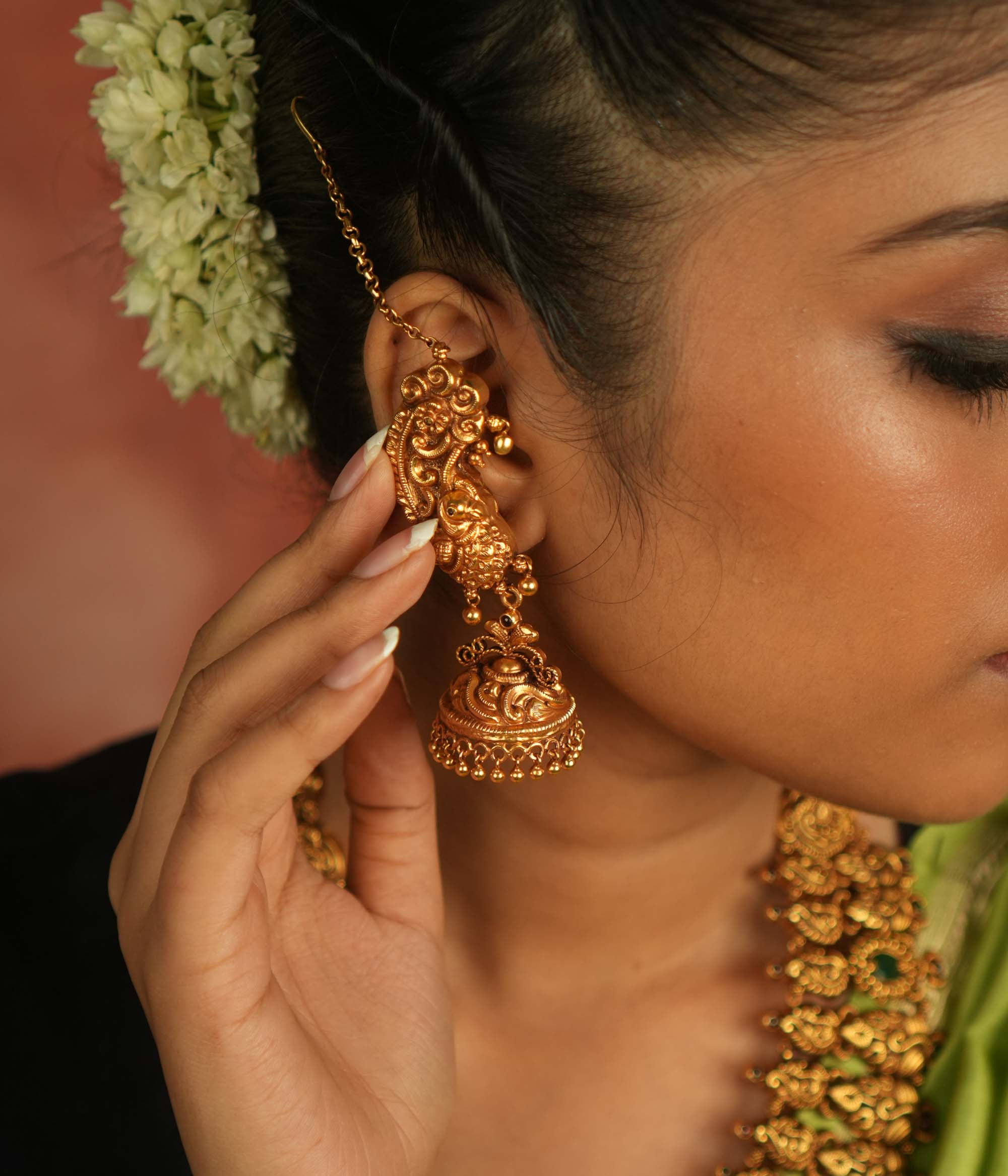Regal peacock reborn! This gold-plated temple jhumka features intricate peacock motifs and a vibrant red spinel stone, with a delicate ear chain of tiny golden beads. A timeless blend of avian artistry and cultural opulence.
