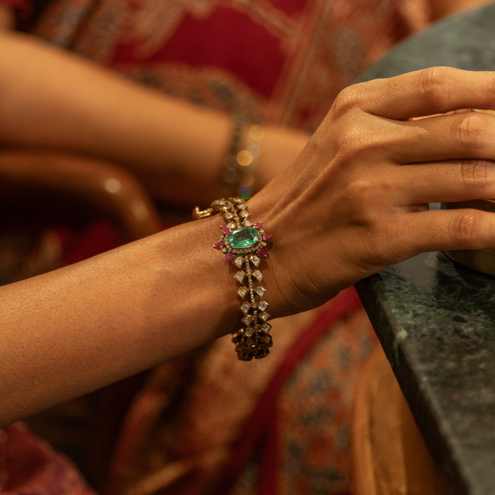 Gold Victorian bangle with a central green gemstone, surrounding polki and CZ stones, worn on a woman's wrist.