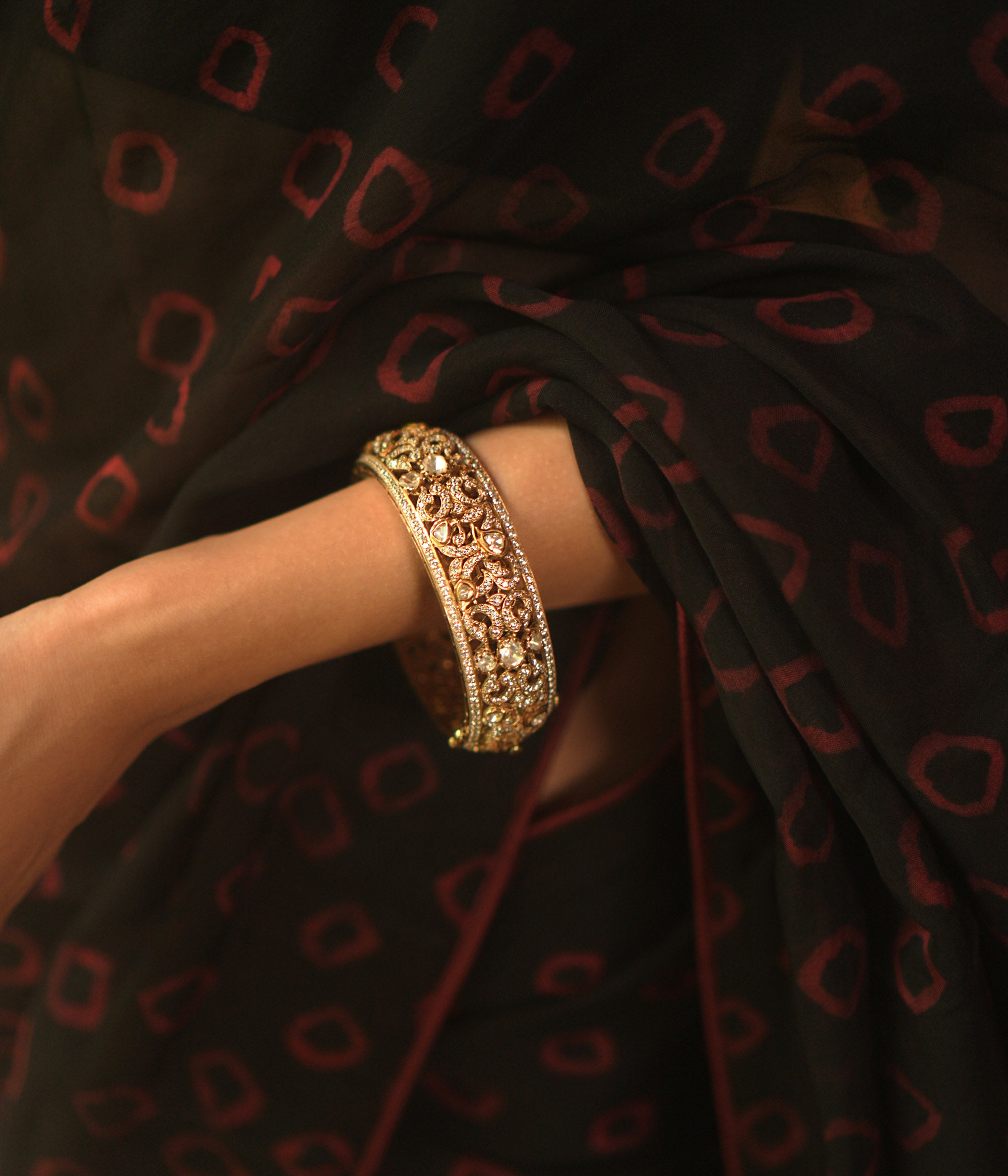 A gold bangle with intricate filigree and royal carvings.