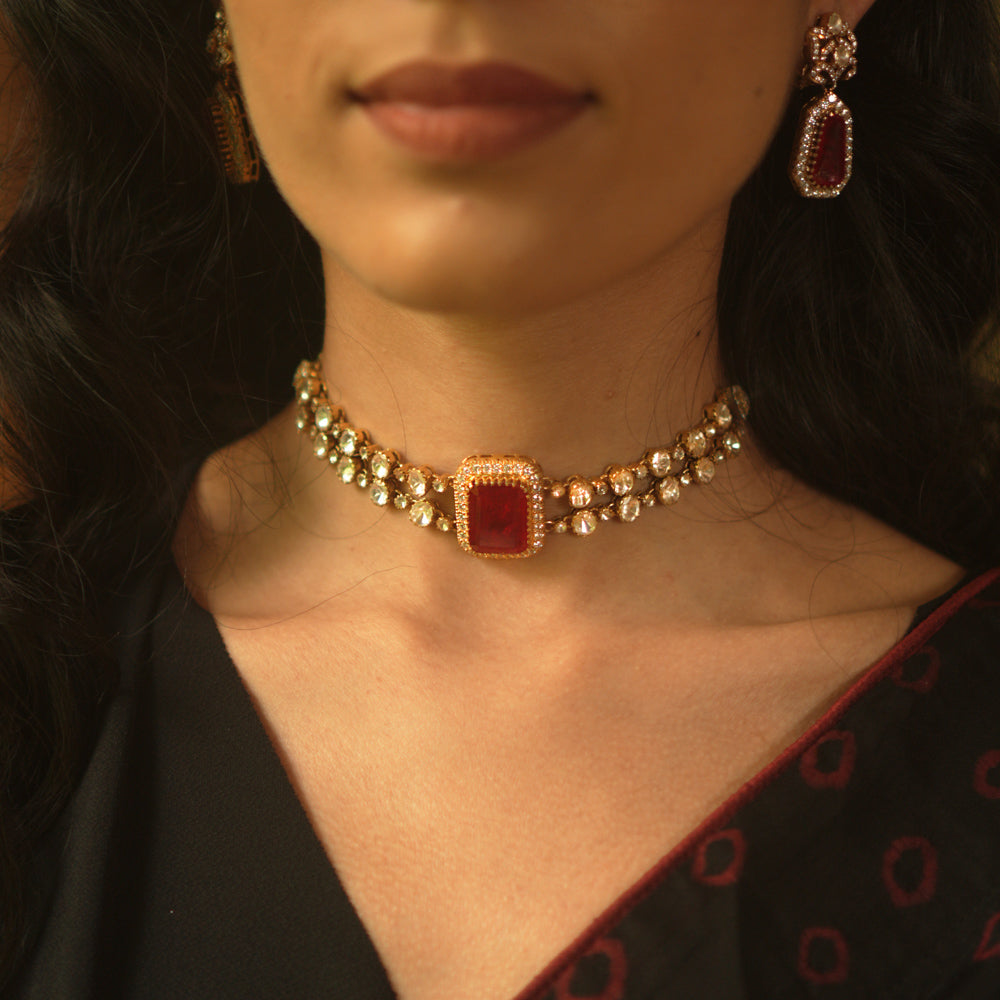 A gold choker with a central rectangular crimson stone, flanked by two rows of small clear stones, worn on a person's neck.