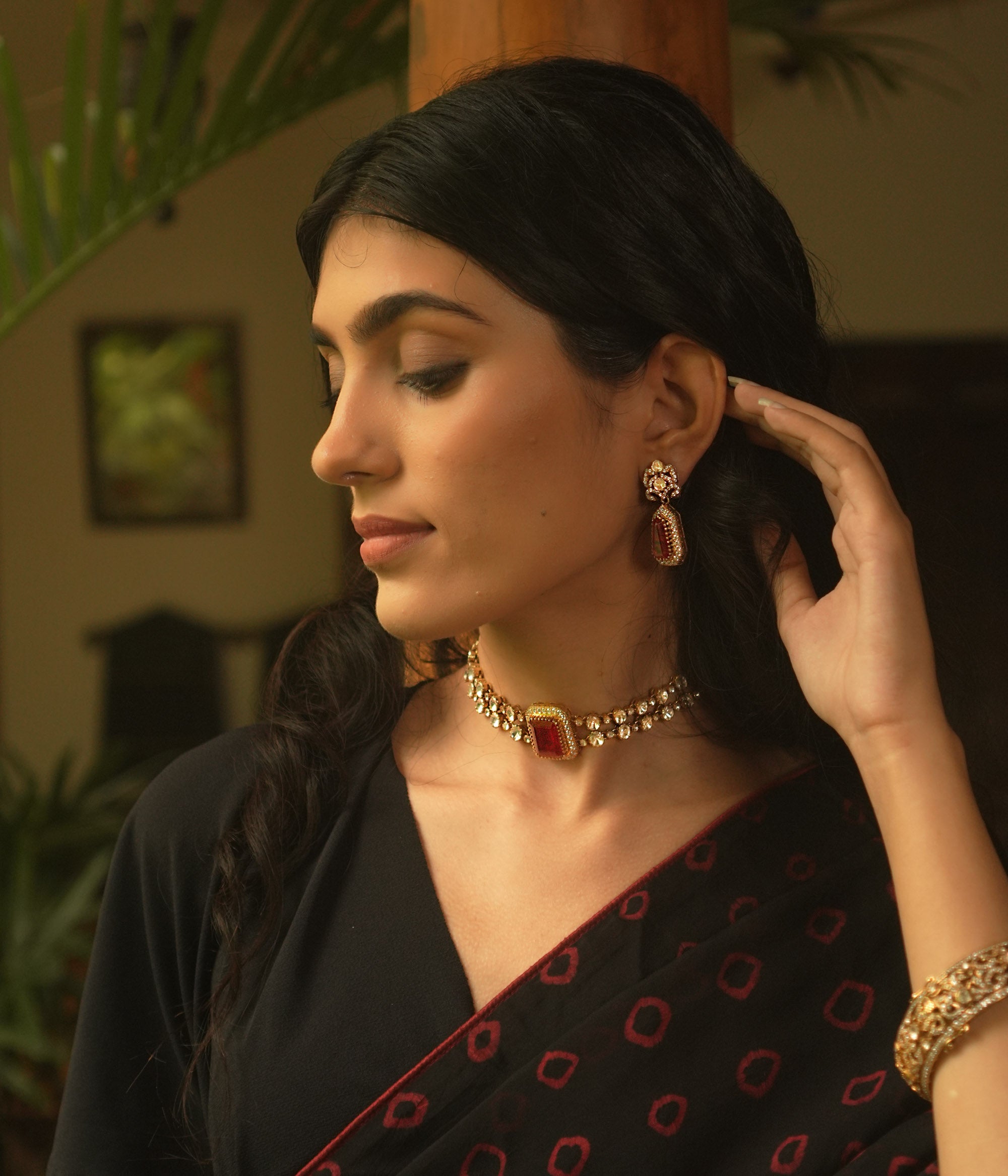 A gold choker with a central rectangular crimson stone, flanked by two rows of small clear stones, worn on a person's neck.