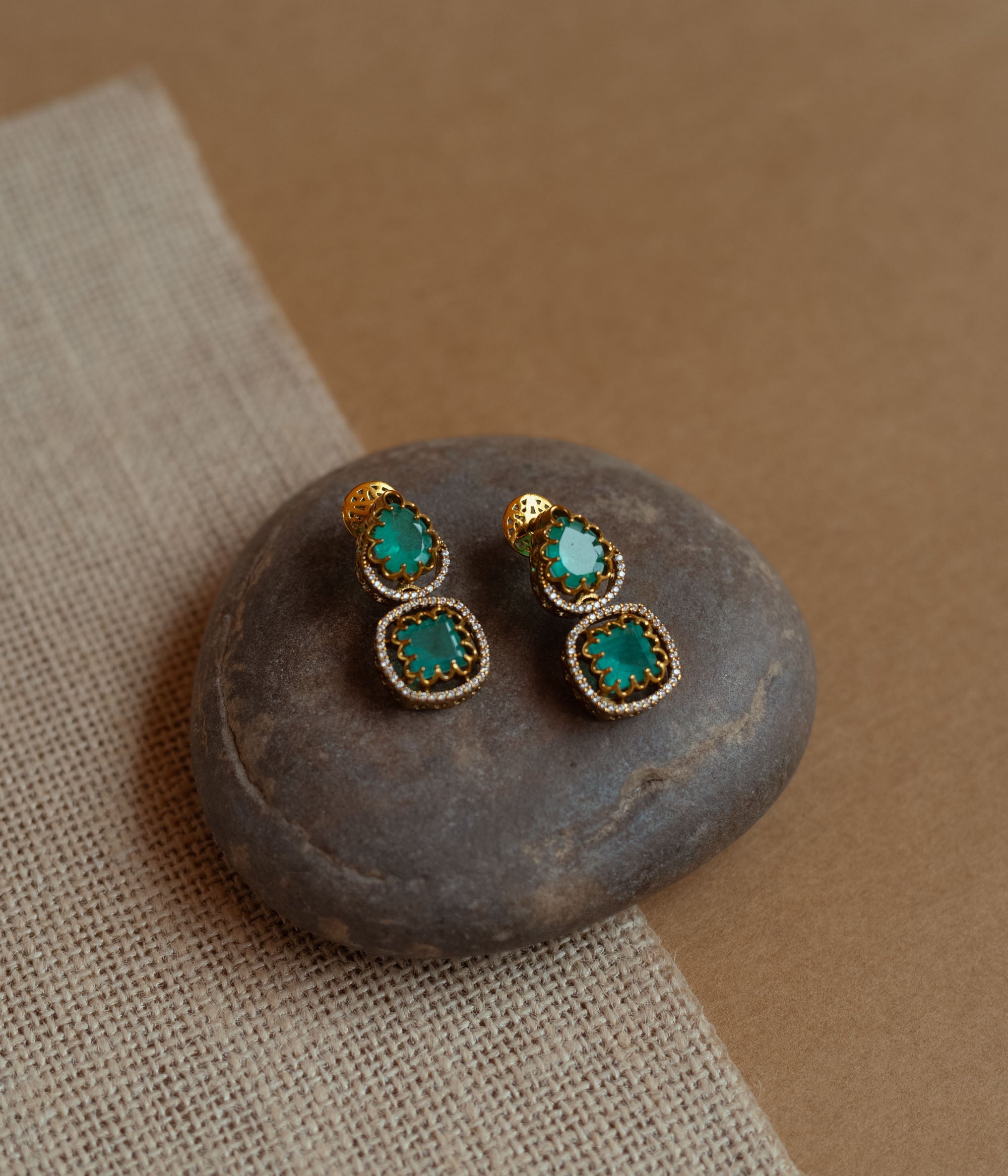 Gold drop earrings with green gemstones surrounded by CZ stones, worn by a woman.