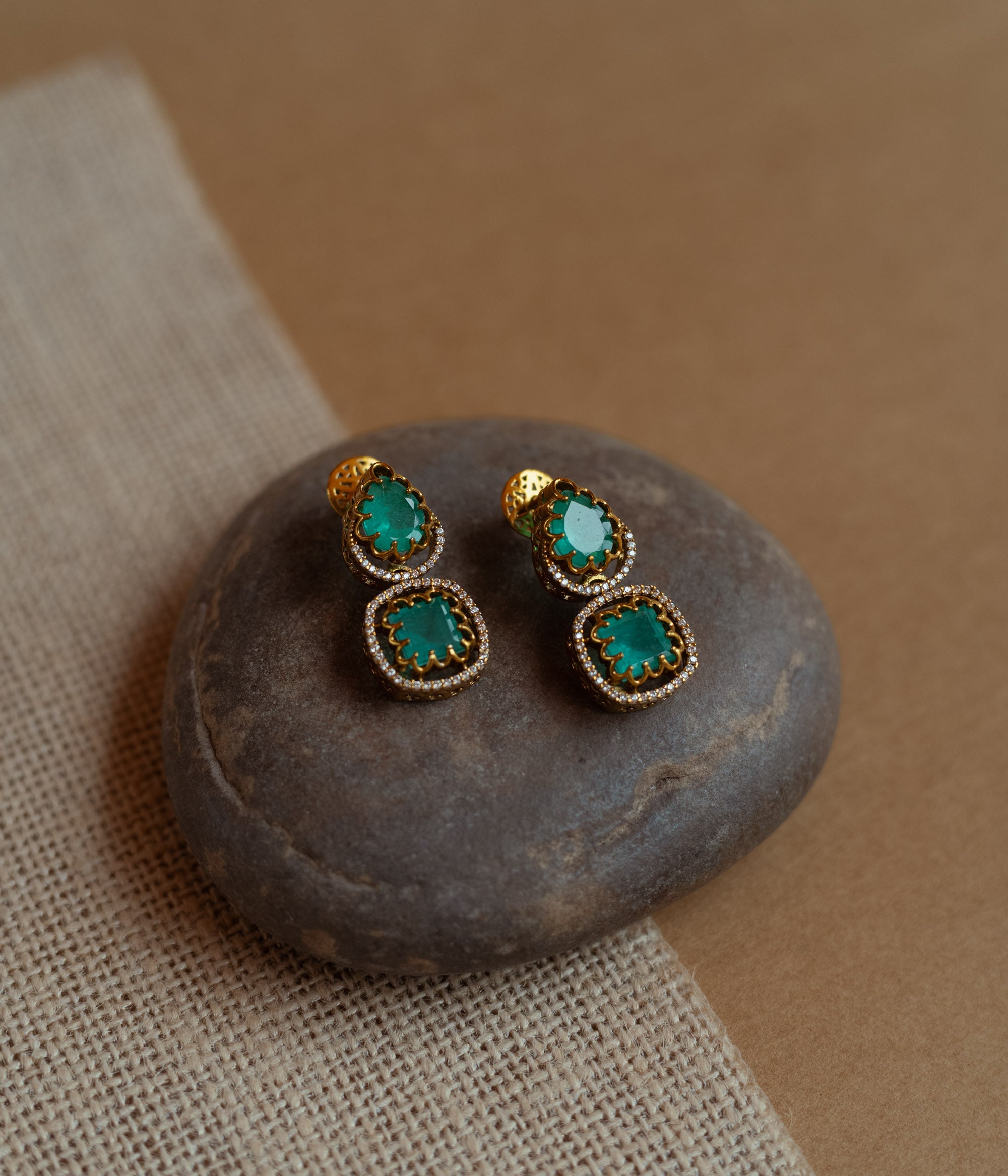 Gold drop earrings with green gemstones surrounded by CZ stones, worn by a woman.