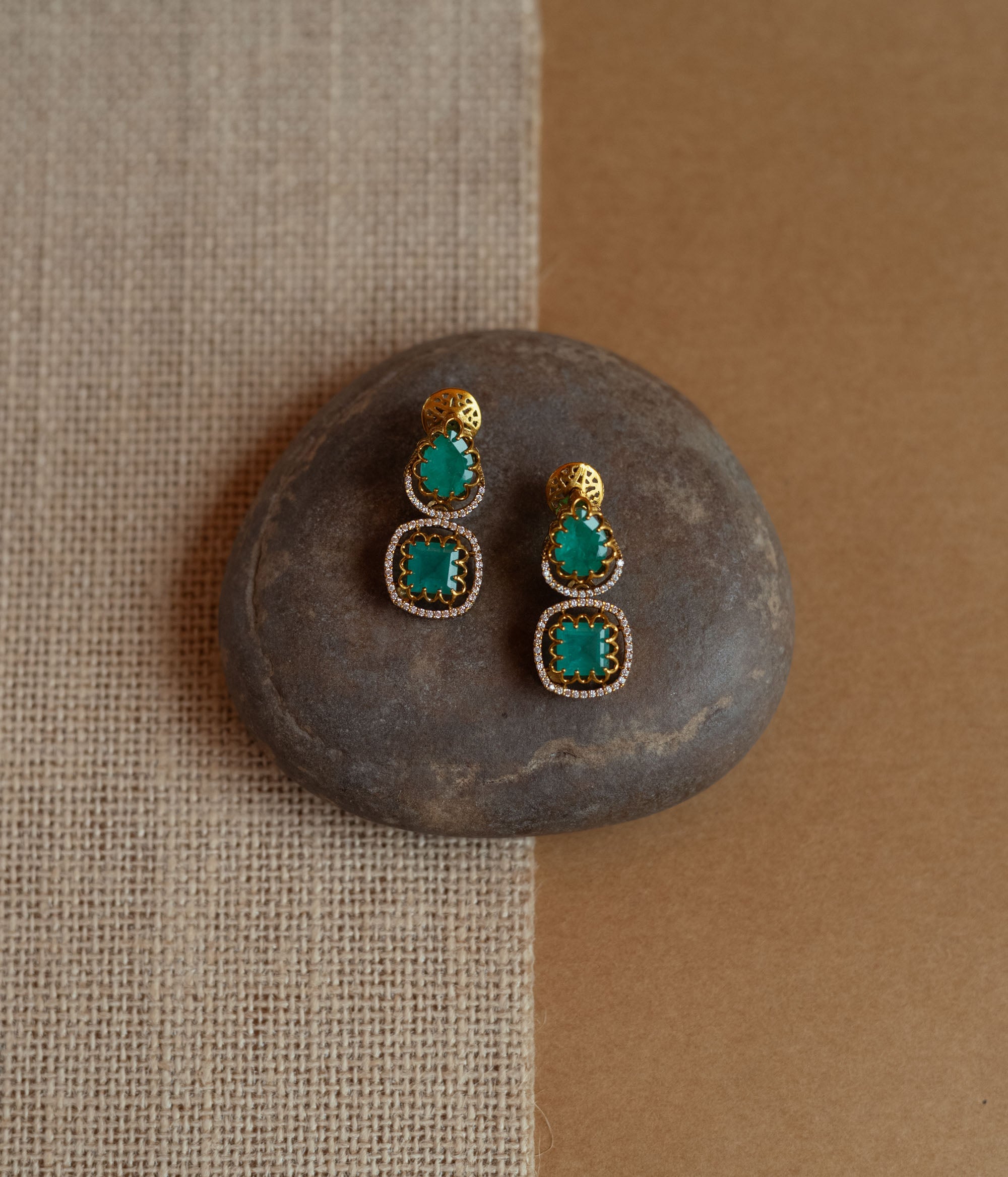 Gold drop earrings with green gemstones surrounded by CZ stones, worn by a woman.