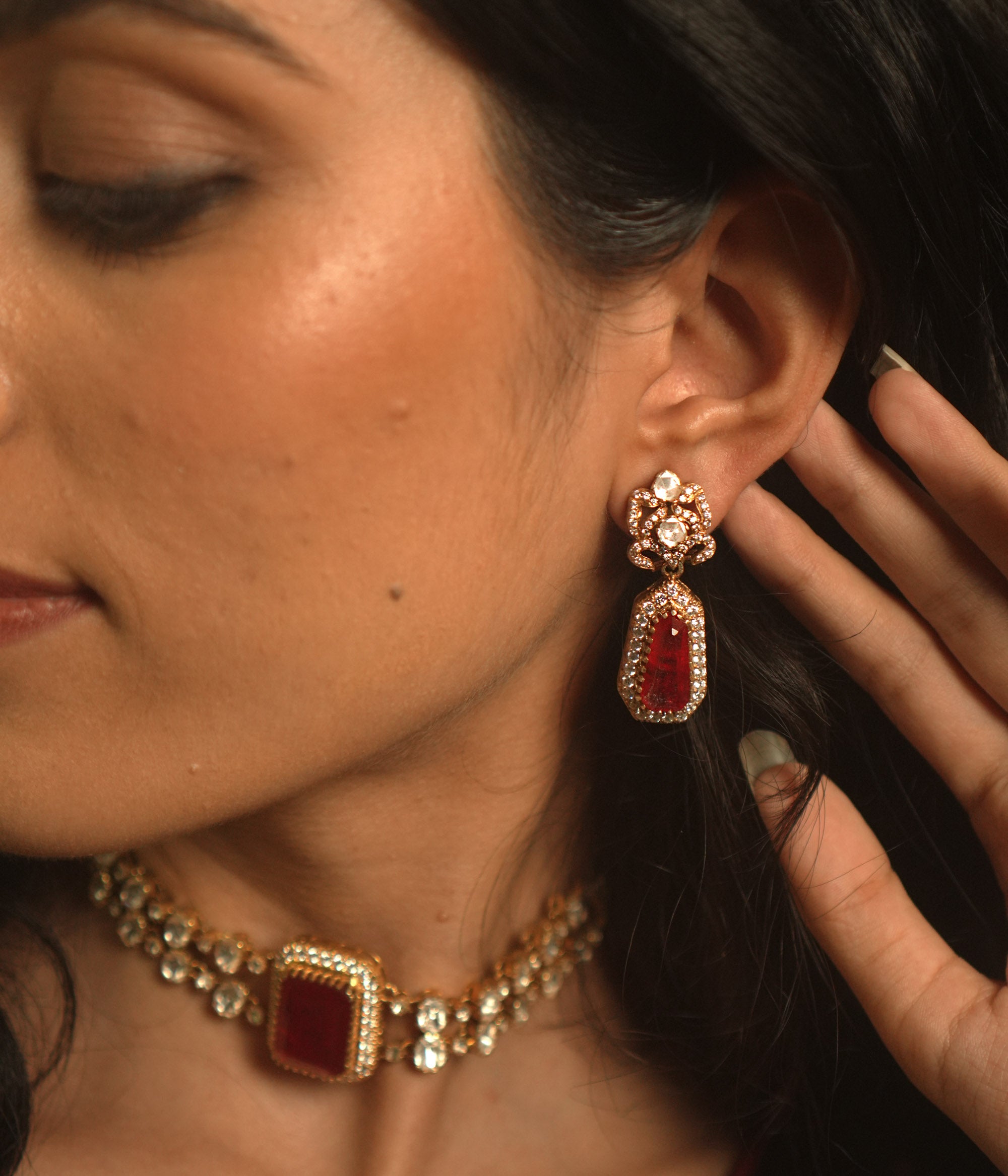 Gold earrings with a floral top, a large red stone, and a drop of white moissanite.