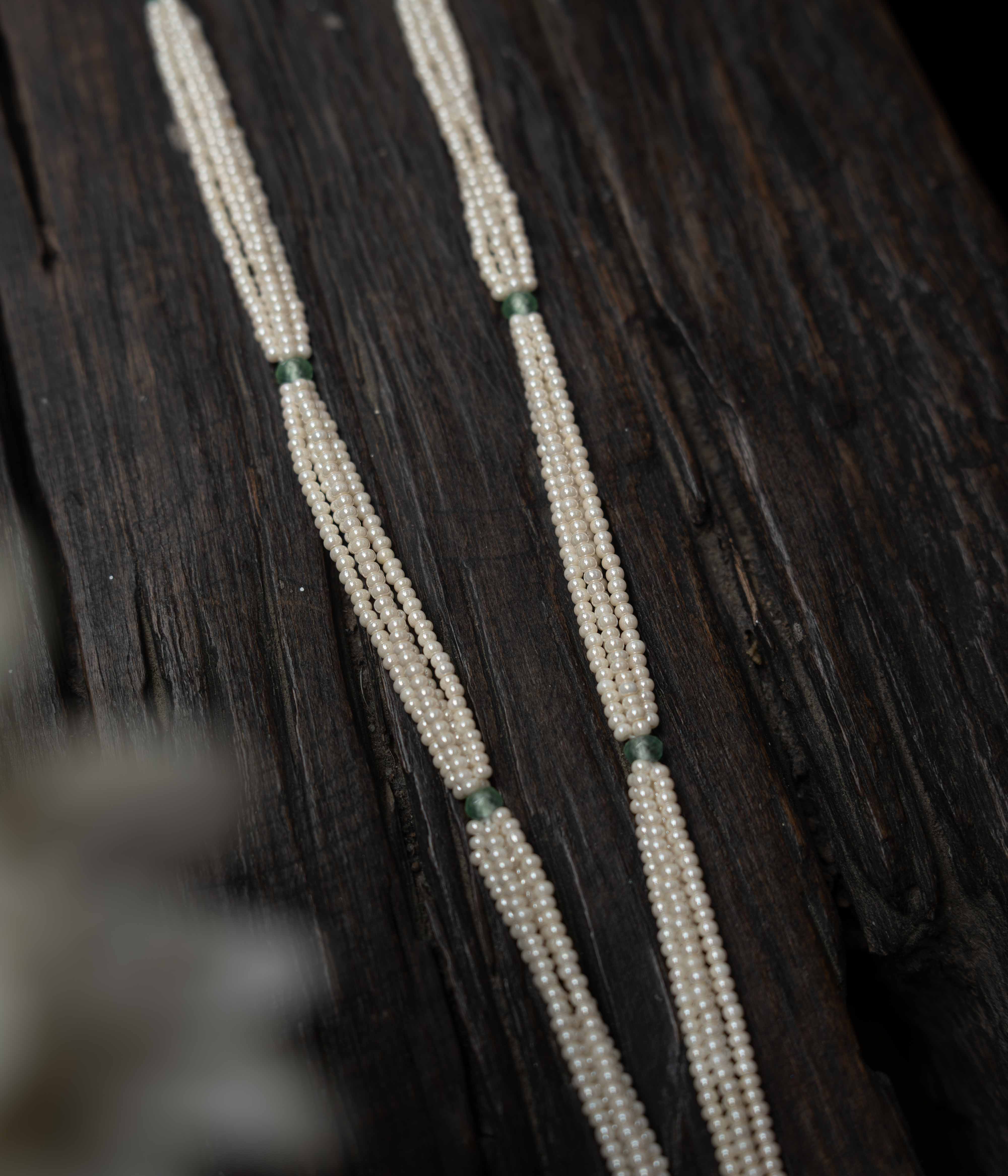 An intricate choker-style necklace with a green gem centerpiece, clear stones, and pearl drops.