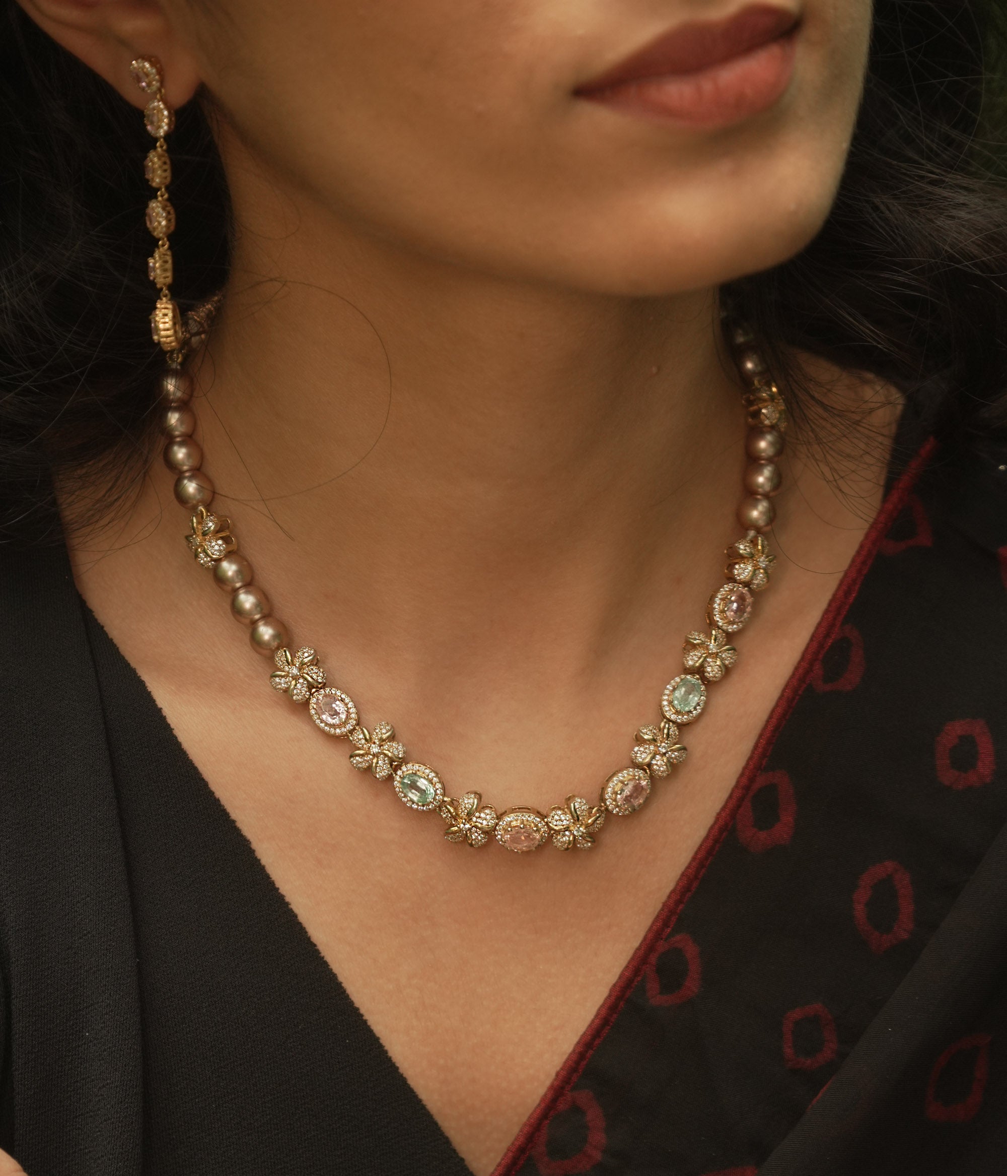 A necklace with multiple strands of pearls and three round, floral medallions with red and green stones.
